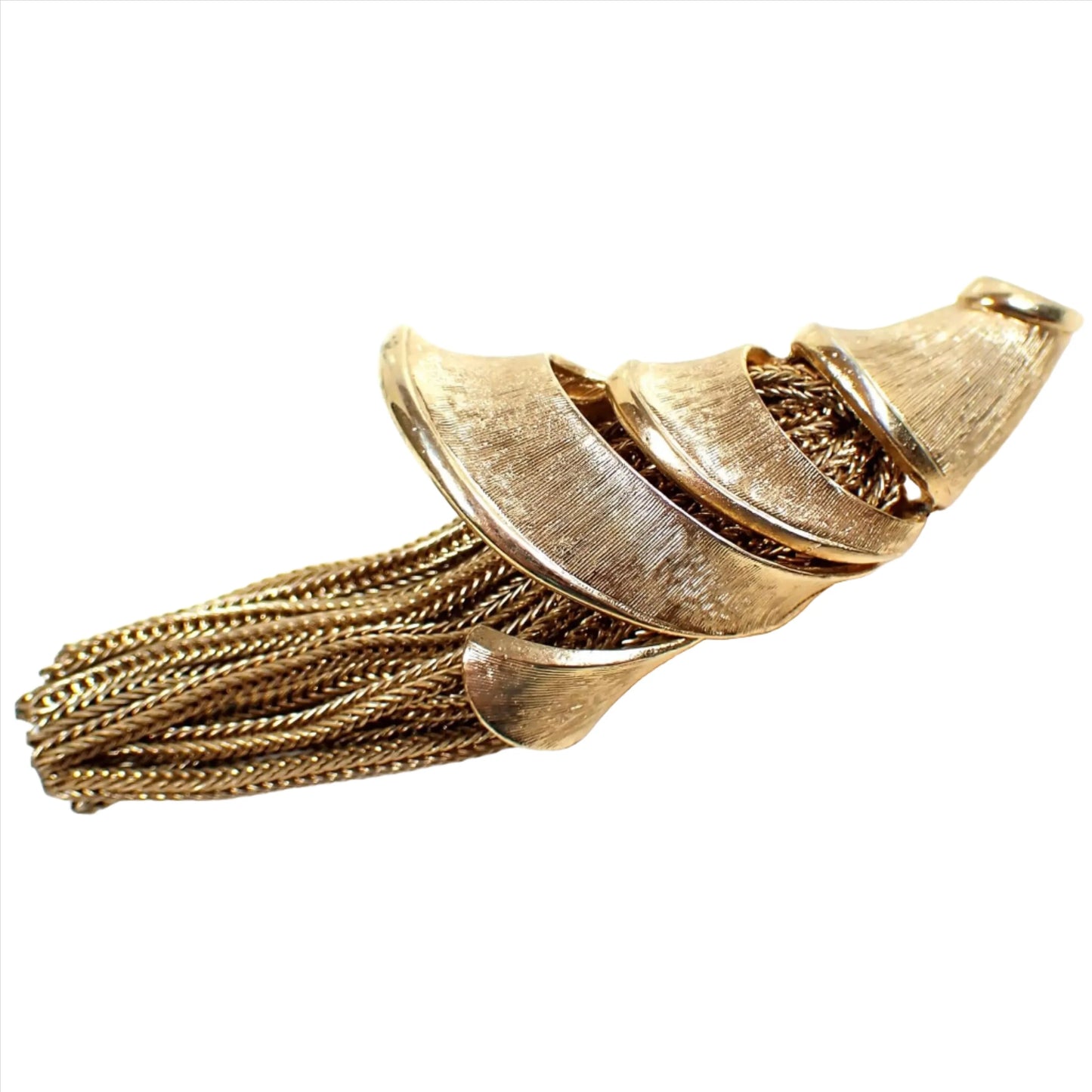 Angled side view of the Mid Century vintage tassel brooch pin. There is a cone shell or horn of plenty type shape wound around the top part of the brooch. There are braided strands of wheat chain coming out of the bottom of the brooch to form the tassel. The metal is gold tone in color and has a matte brushed appearance.