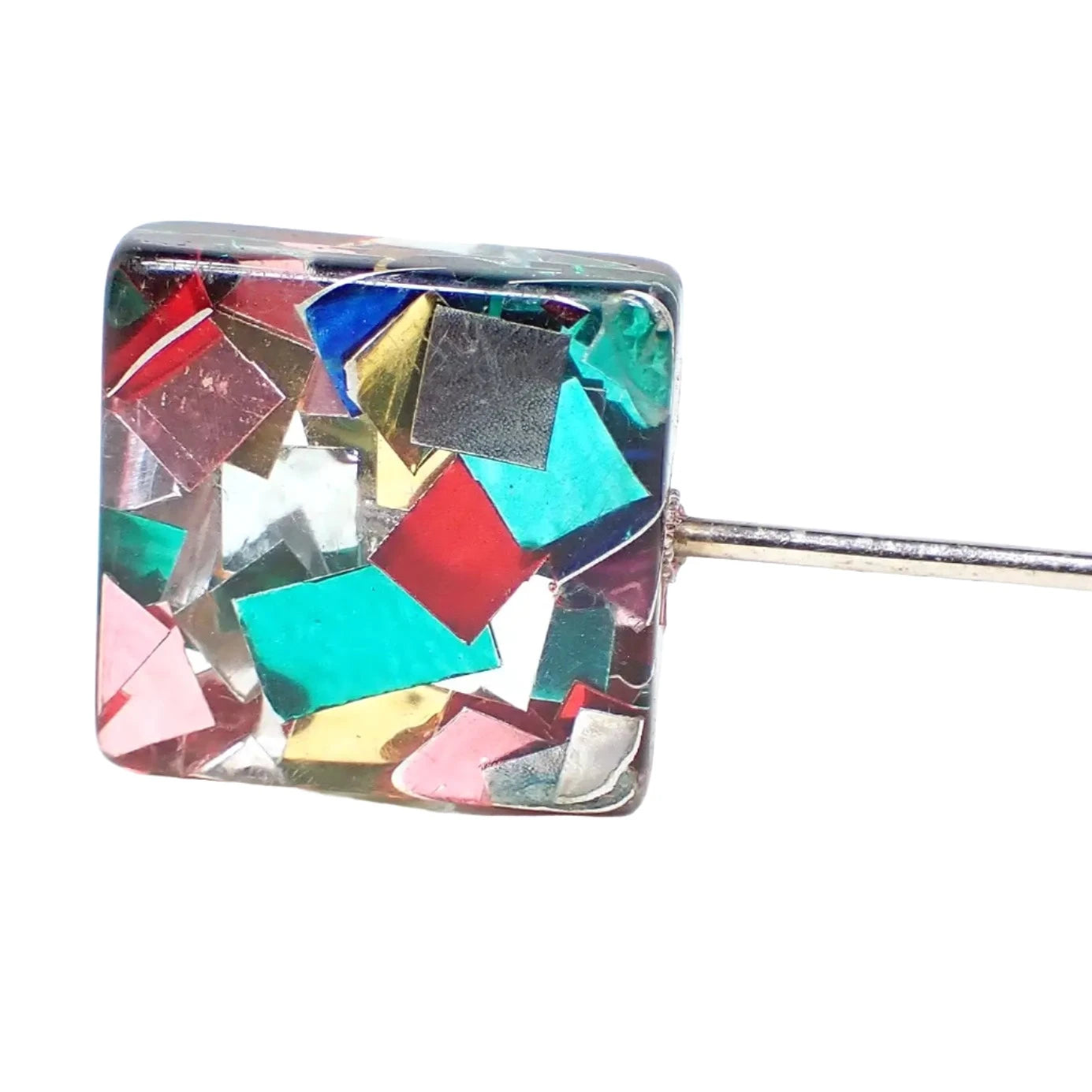 Enlarged view of the top of the pre owned stick pin. It is square in shape with clear resin. Embedded in the rest are square and rectangular shaped pieces of colored thin metal for a rainbow multi color appearance.