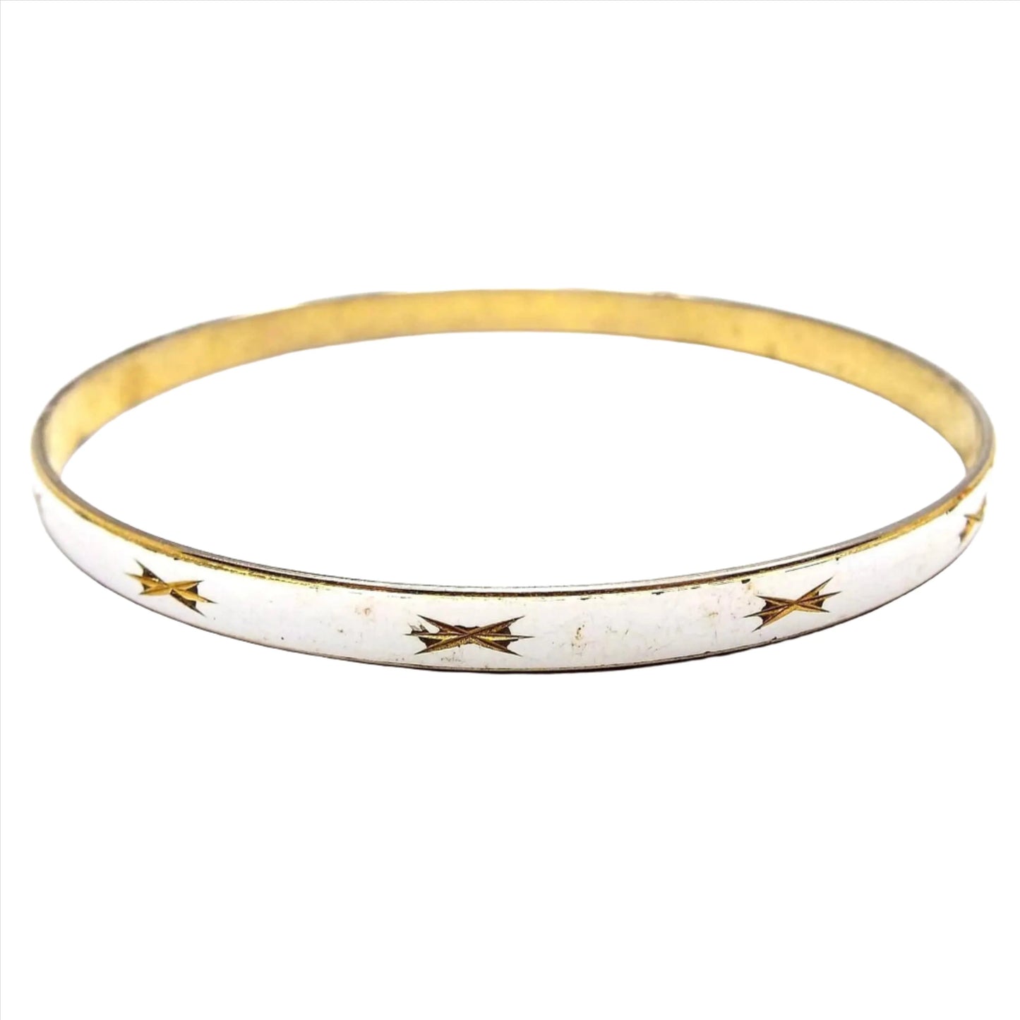 Front view of the Mid Century vintage Japanese bangle bracelet. The metal is gold tone in color. The outside edge is enameled white and has a cut starburst style design around the bracelet. There is some tiny chips and wear to the enamel.