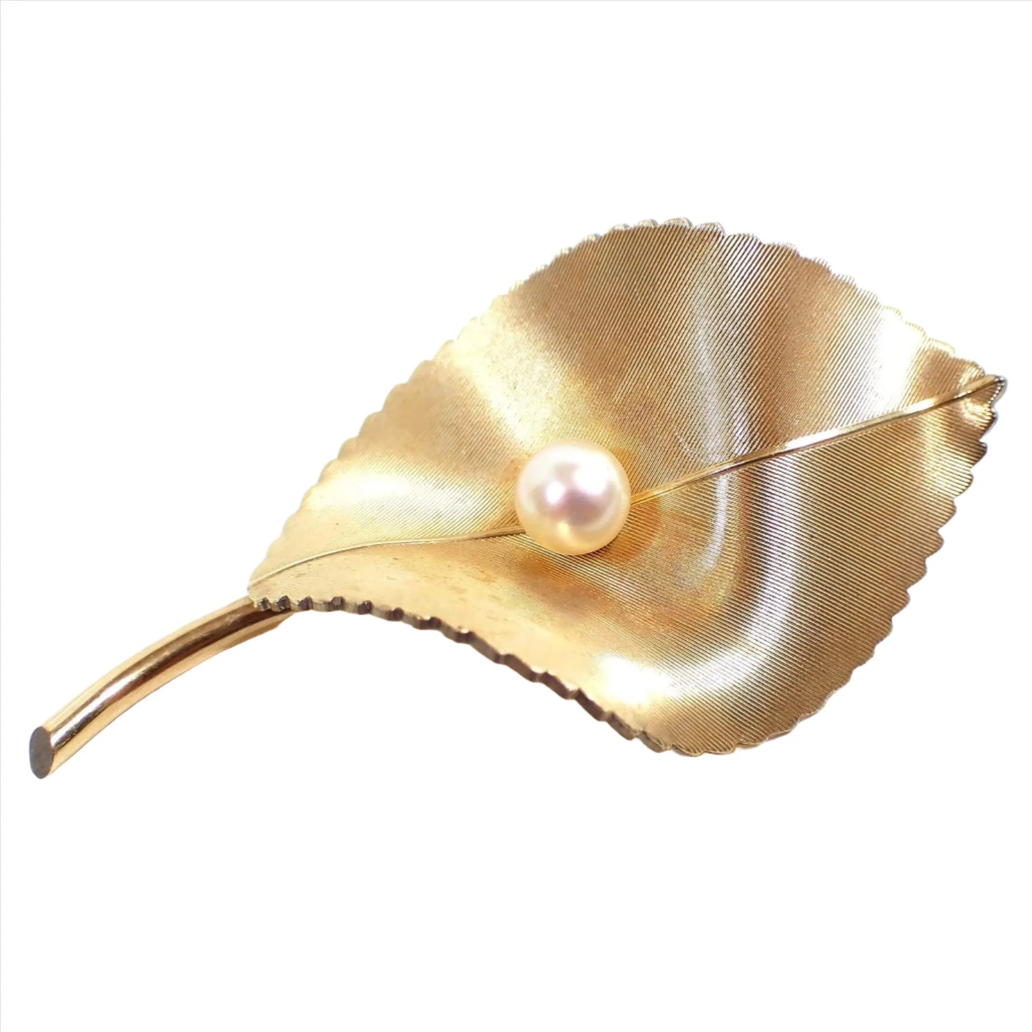 Front view of the Mid Century vintage Krementz brooch pin. The metal is a matte brushed textured gold tone plated in color. The brooch is shaped like a curvy leaf with a stem and scalloped edges on the sides. There is a cultured pearl in the middle of the leaf.