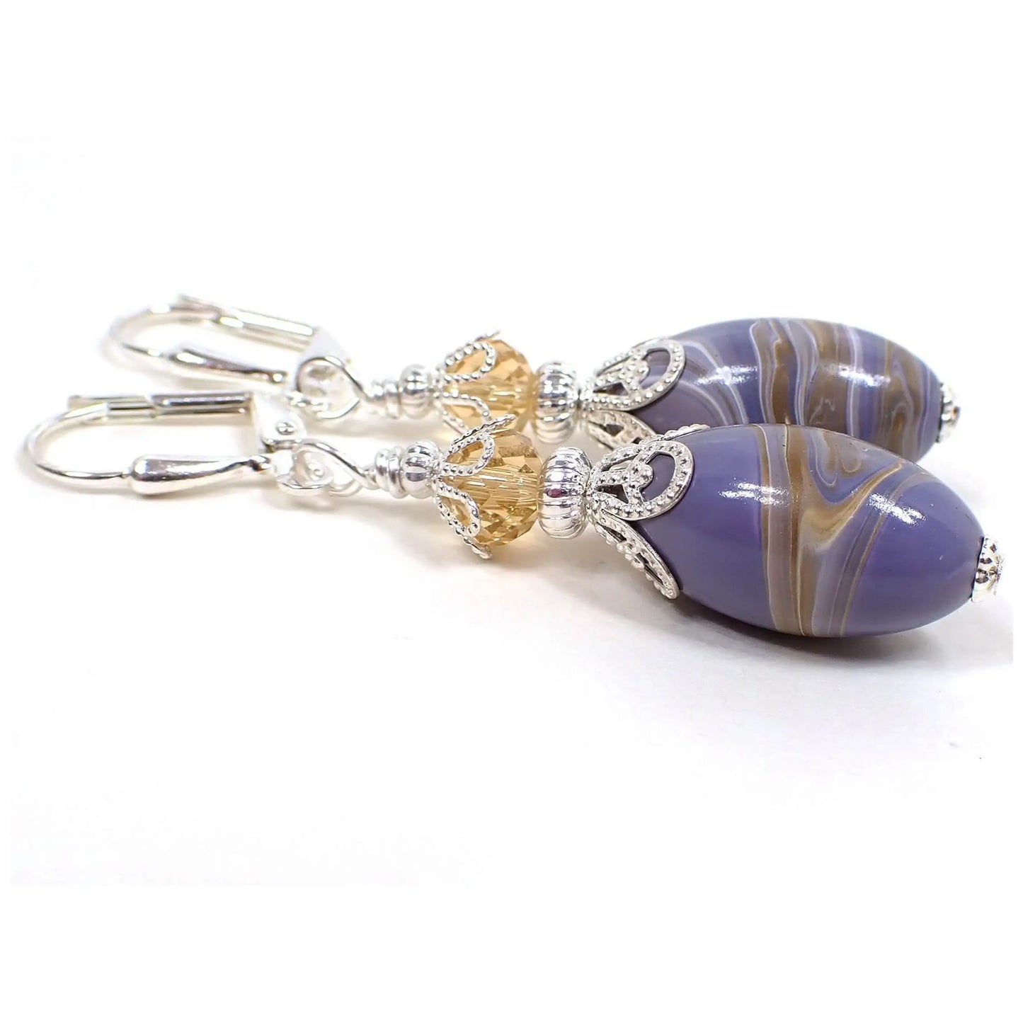 Side view of the handmade earrings with vintage lucite beads. The metal is silver plated in color. There are light golden color faceted glass crystal beads at the top. The bottom lucite beads are oval shaped and have marbled swirls of pastel purple, shades of brown, and white.