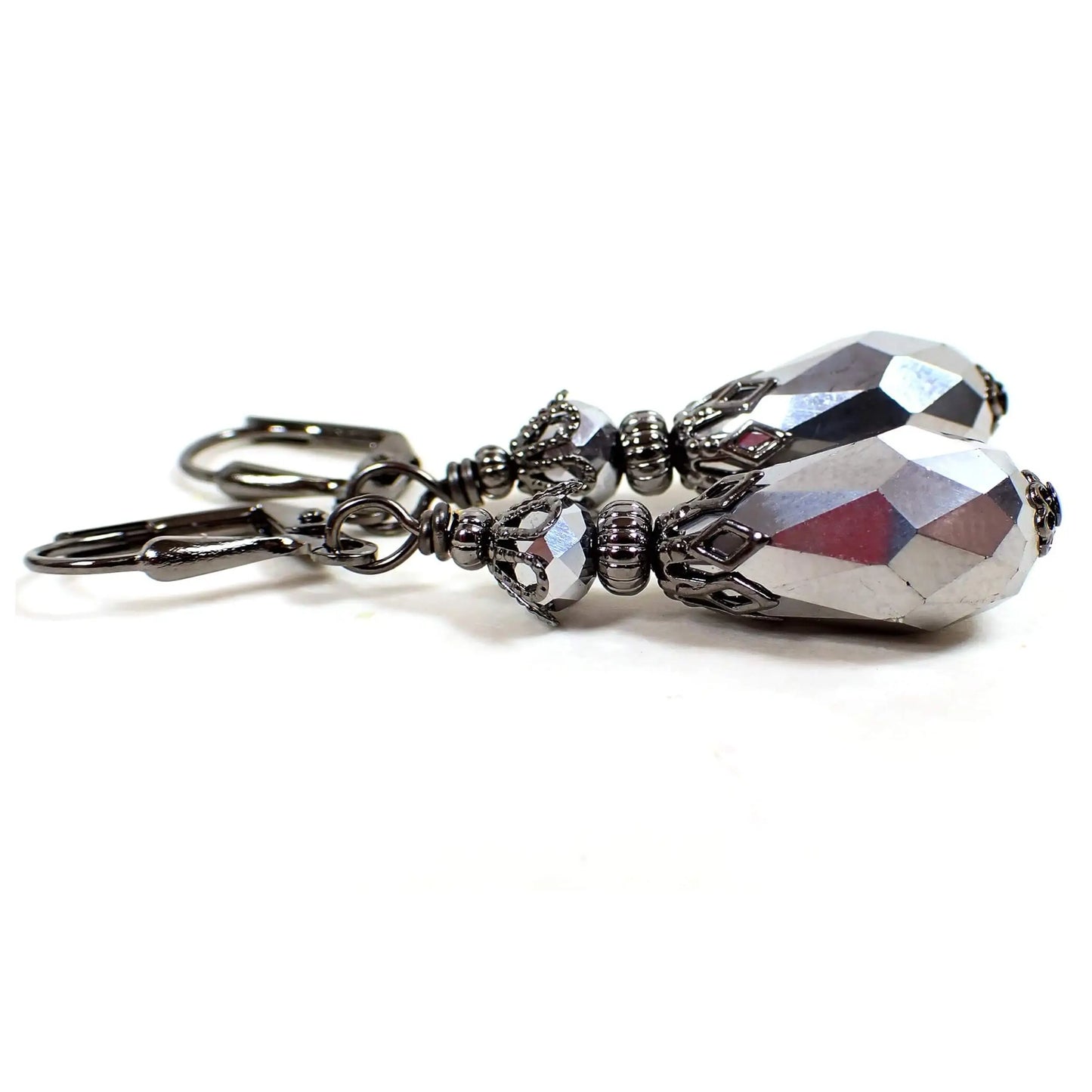 Side view of the handmade teardrop earrings. The metal is gunmetal gray in color. There are rondelle shaped faceted glass beads at the top. The bottom beads are faceted teardrop shaped and both are metallic dark silver in color.