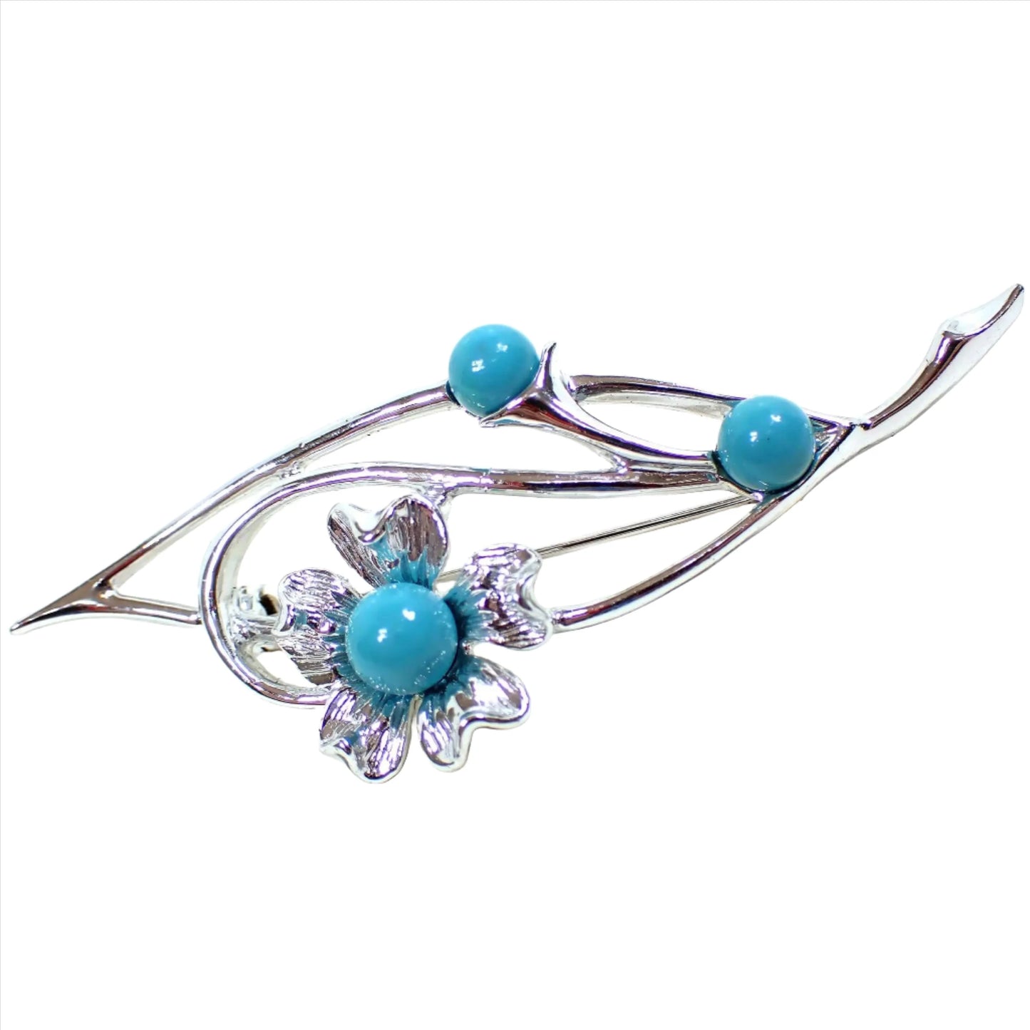 Angled front view of the Mid Century vintage Sarah Coventry floral brooch pin. The metal is silver tone in color. There is an angled open leaf like shape with a curled area and a flower at the end. There are three turquoise blue color cabs on the brooch, including one in the middle of the flower.