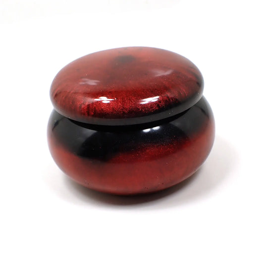 Side view of the Goth small handmade resin trinket box. It's shaped like a rounded rondelle jar with rounded top. There is pearly red resin at the top and bottom of the piece and pearly black resin in the middle.