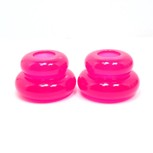 Side view of the pair of handmade double ring candlestick holders. They are shaped like puffy donut rings with a larger one on bottom and a smaller one on top. The resin is bright neon pink in color. There is a round hole at the top for the candlesticks to go in.