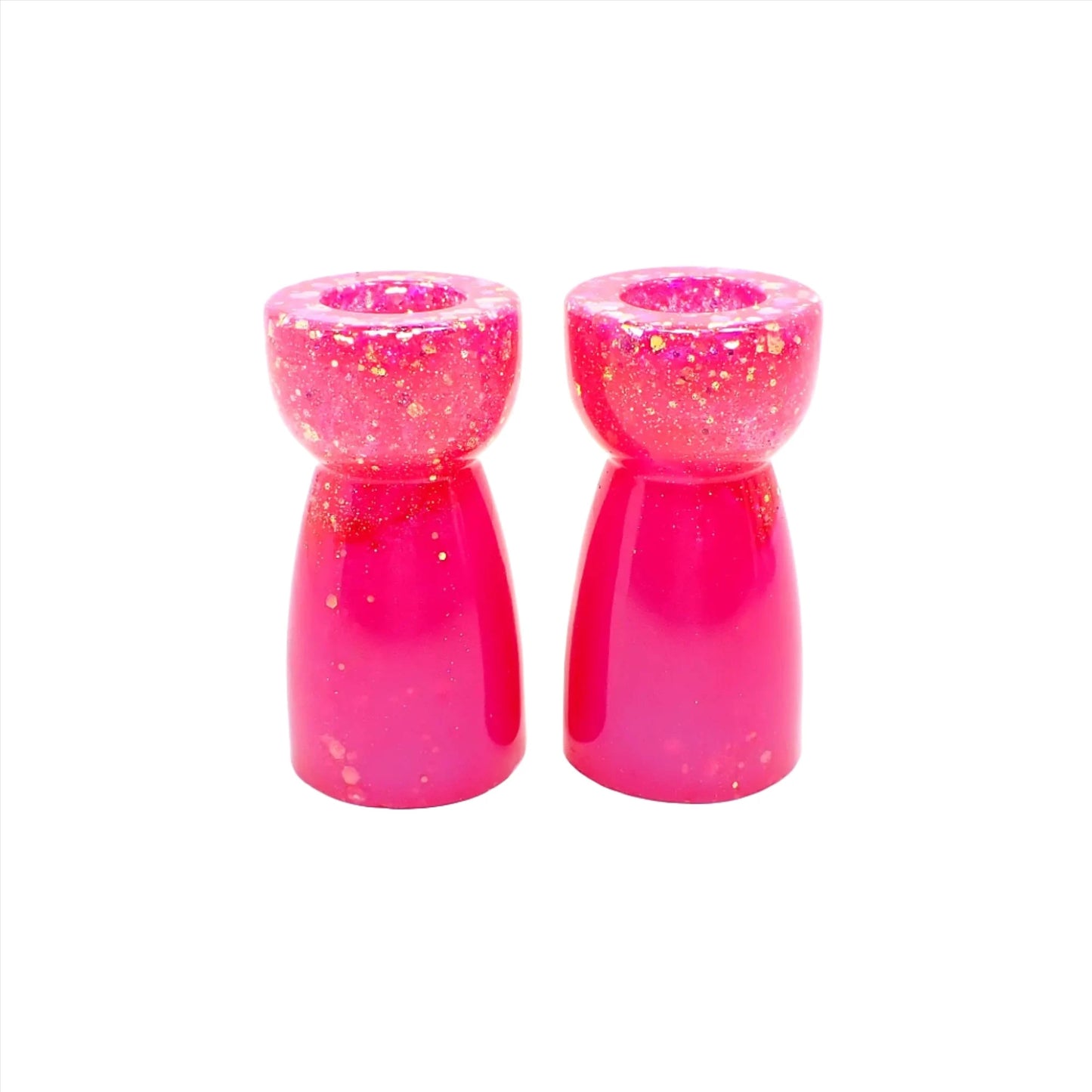 Side view of the handmade resin candlestick holders. They have bright pearly pink resin and chunky iridescent glitter. The glitter shows mostly at the top portion of the pieces. They are rounded on top and a cone like shape underneath that flares out to the bottom.