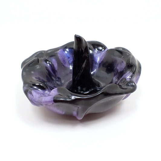 Angled view of the handmade resin ring dish holder. It's shaped like a flower with the petals open and one in the middle sticking up for the rings to set on. It has pearly black resin with a slight color shift resin marbled in. The color shift resin is mostly purple, but gives flashes of blue as you move around it in brighter settings.