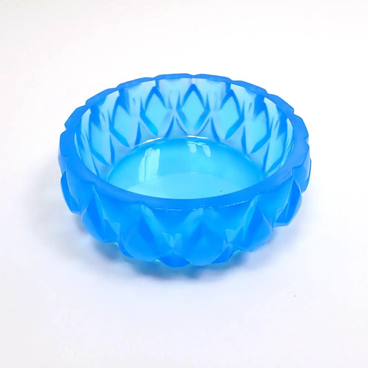 Side view of the small handmade short round succulent pot. It has a short round shape with bright neon blue resin. There is a diamond shaped pattern going all the way around. The large opening on top is wide for putting small plants or using as a trinket dish.