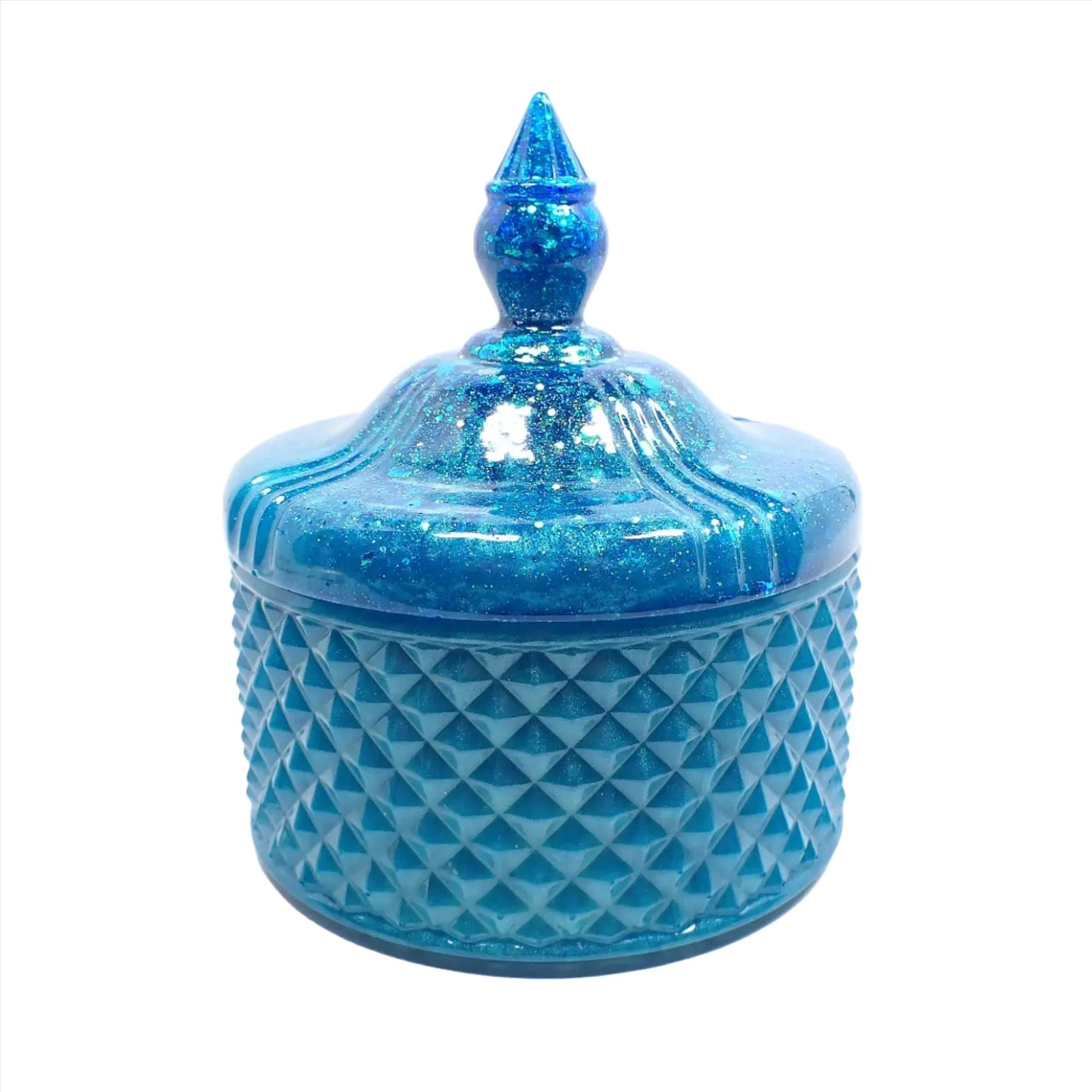 Side view of the handmade large trinket candy dish. It has pearly aqua blue resin with chunky iridescent glitter on the lid. It is round in shape with a textured diamond shape pattern around the sides. The top is pointed to lift the lid off.