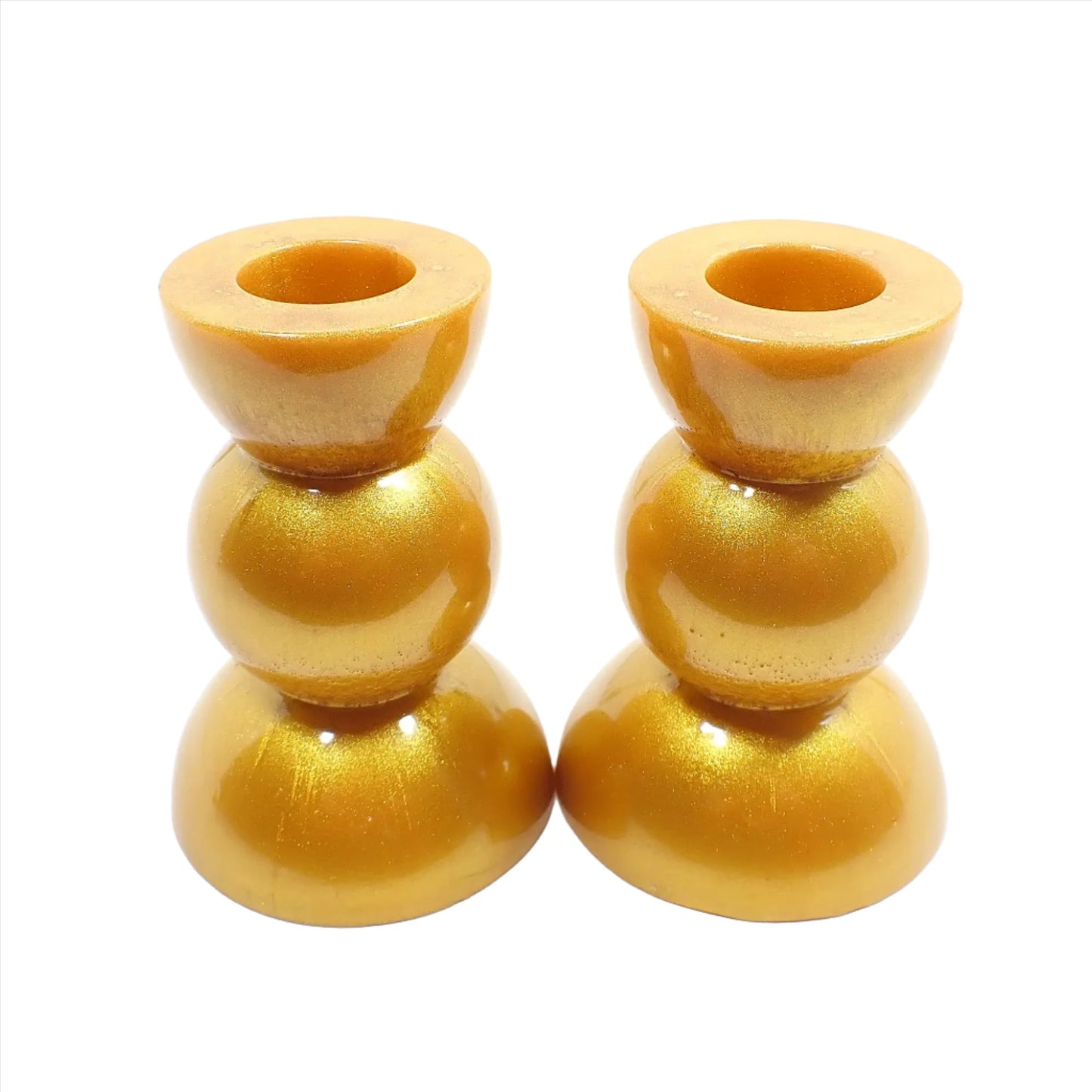 Side view of the handmade geometric candlestick holders. They have a round ball area in the middle and a semi sphere shape on the top and bottom. The resin is a rich shade of pearly metallic gold color.