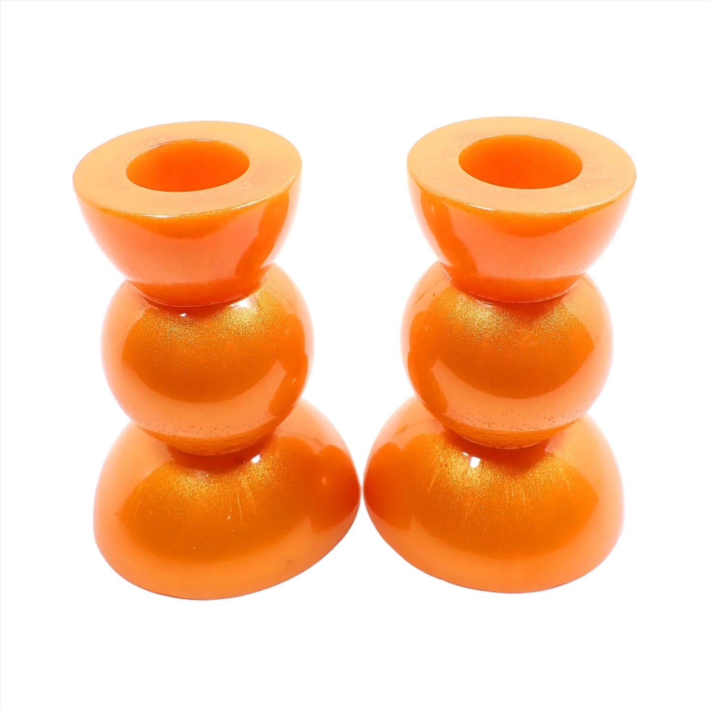 Side view of the handmade geometric candlestick holders. They have a round ball area in the middle and a semi sphere shape on the top and bottom. The resin is a bright citrus orange color with hints of metallic gold.