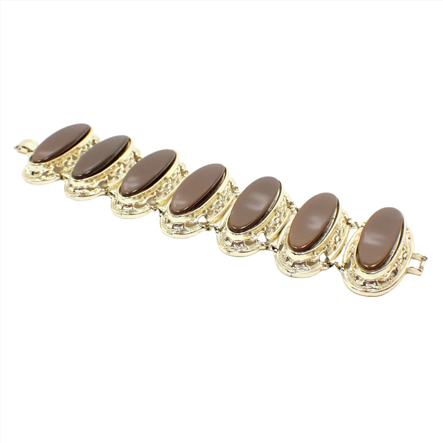 Angled view of the Mid Century vintage wide thermoset link bracelet. The metal is gold tone in color. There are seven large oval links with pearly brown thermoset cabs and filigree settings. There is a snap lock clasp on the end.