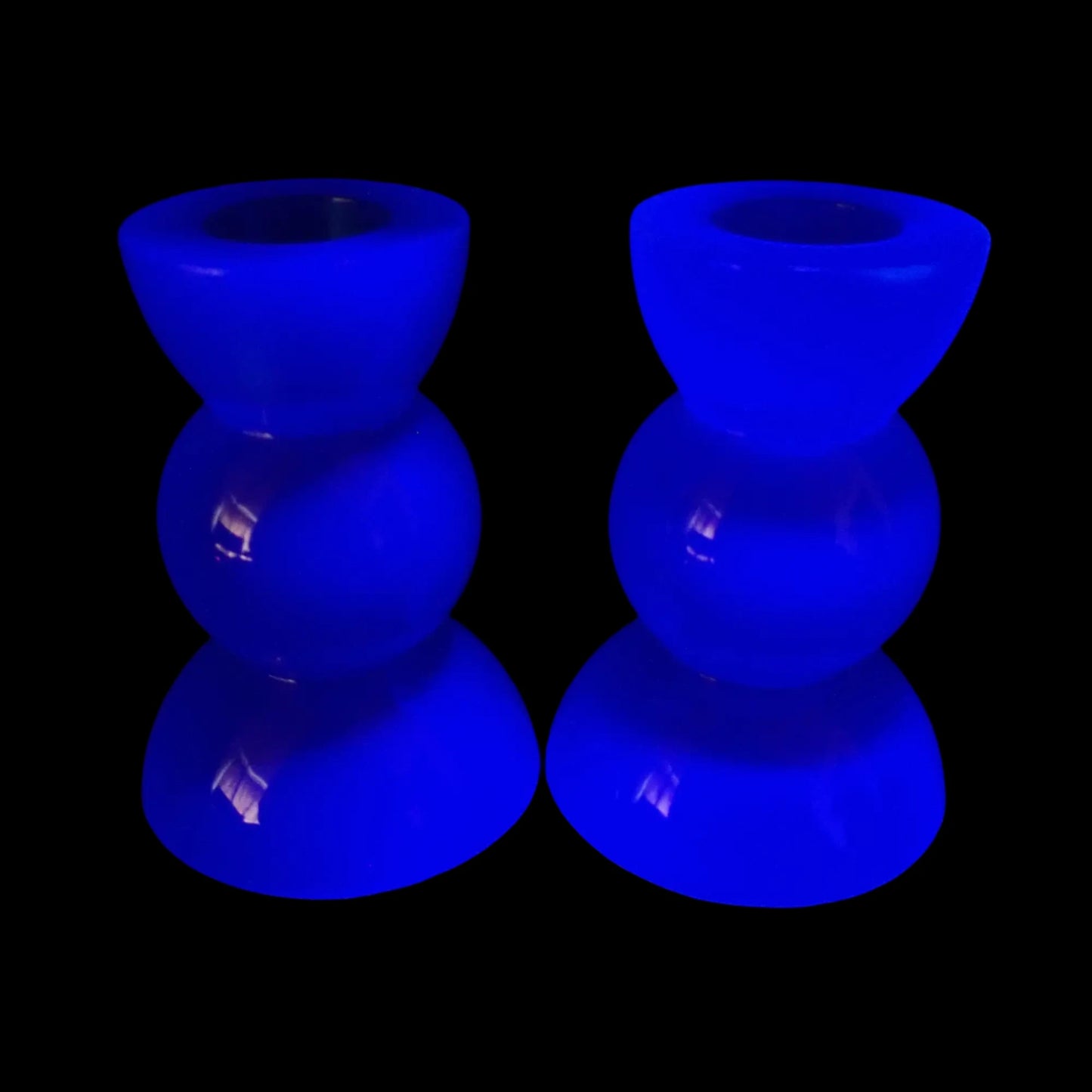 Photo showing the handmade neon blue resin geometric candlestick holders fluorescing under a UV light.