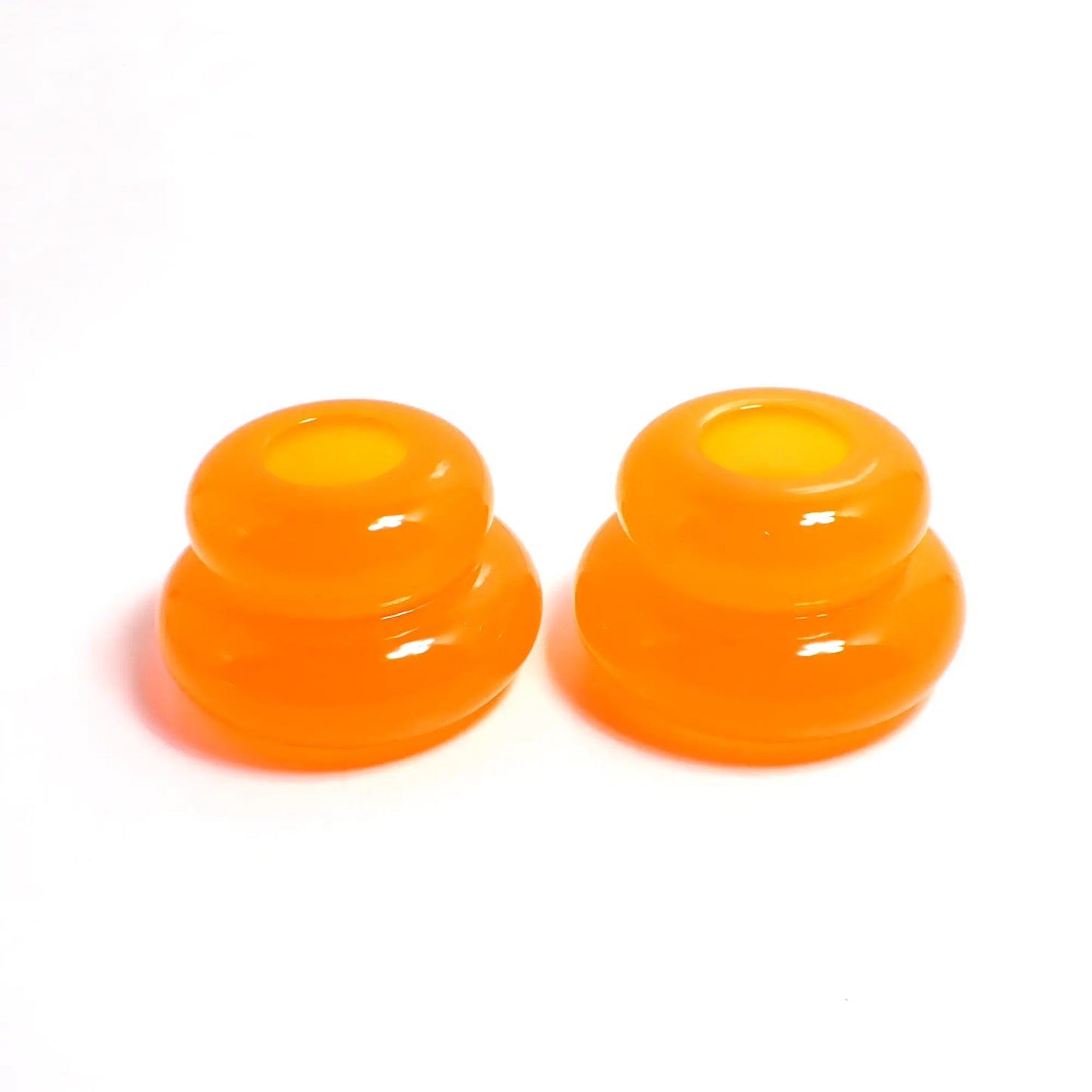 Side view of the pair of handmade double ring candlestick holders. They are shaped like puffy donut rings with a larger one on bottom and a smaller one on top. The resin is neon orange in color. There is a round hole at the top for the candlesticks to go in.