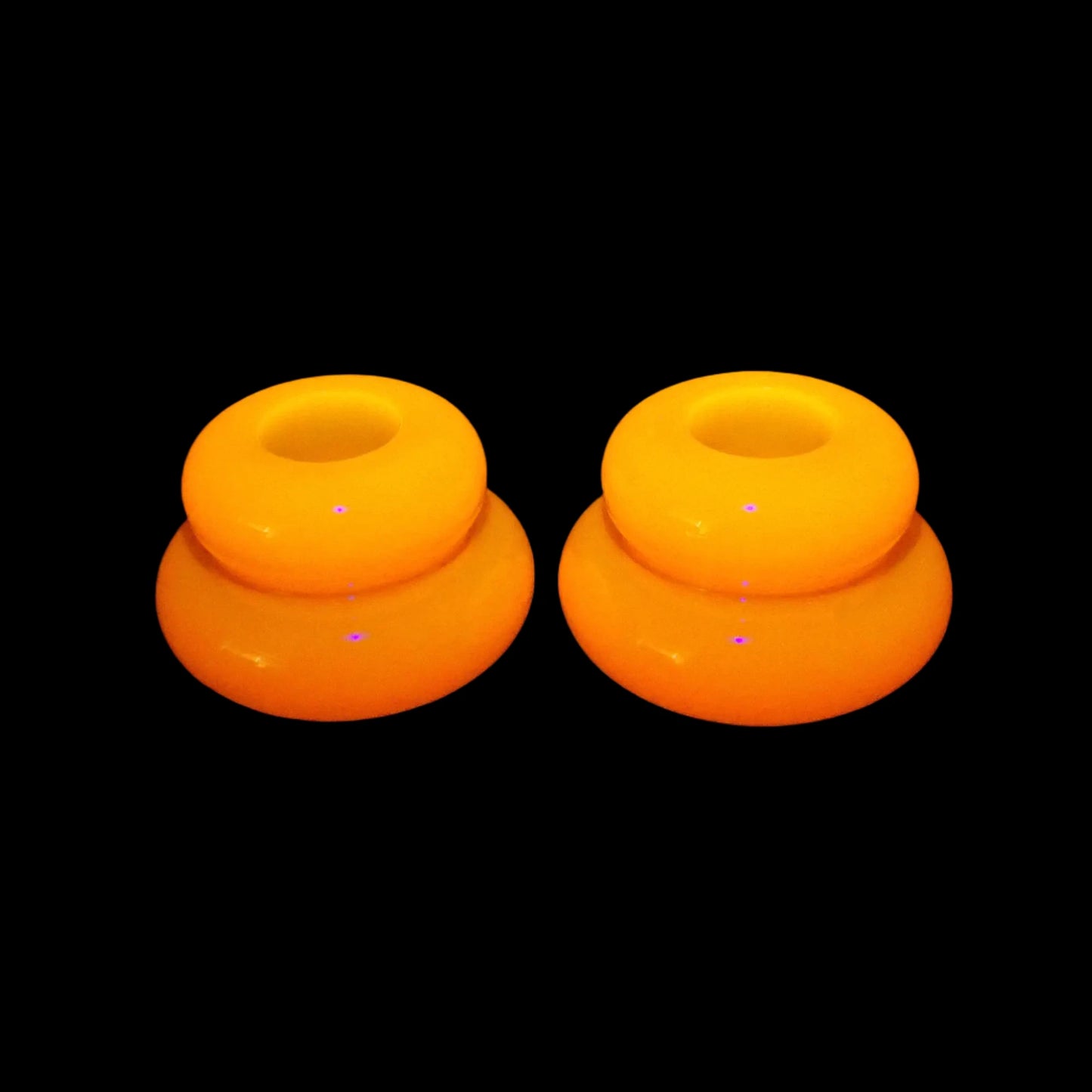 Photo of the handmade resin neon orange puffy round double ring candlestick holders fluorescing bright orange under a UV light.