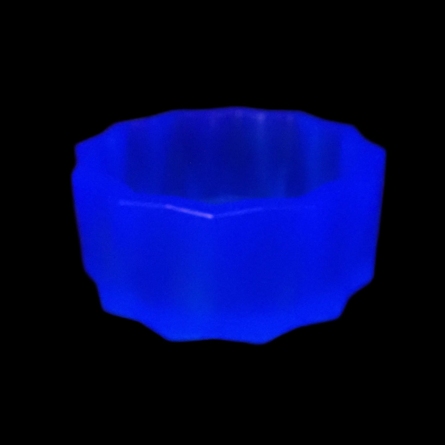 Image of the large handmade neon blue resin facted decorative bowl under a UV light to show that it is fluorescent and glows a bright blue color under the light.