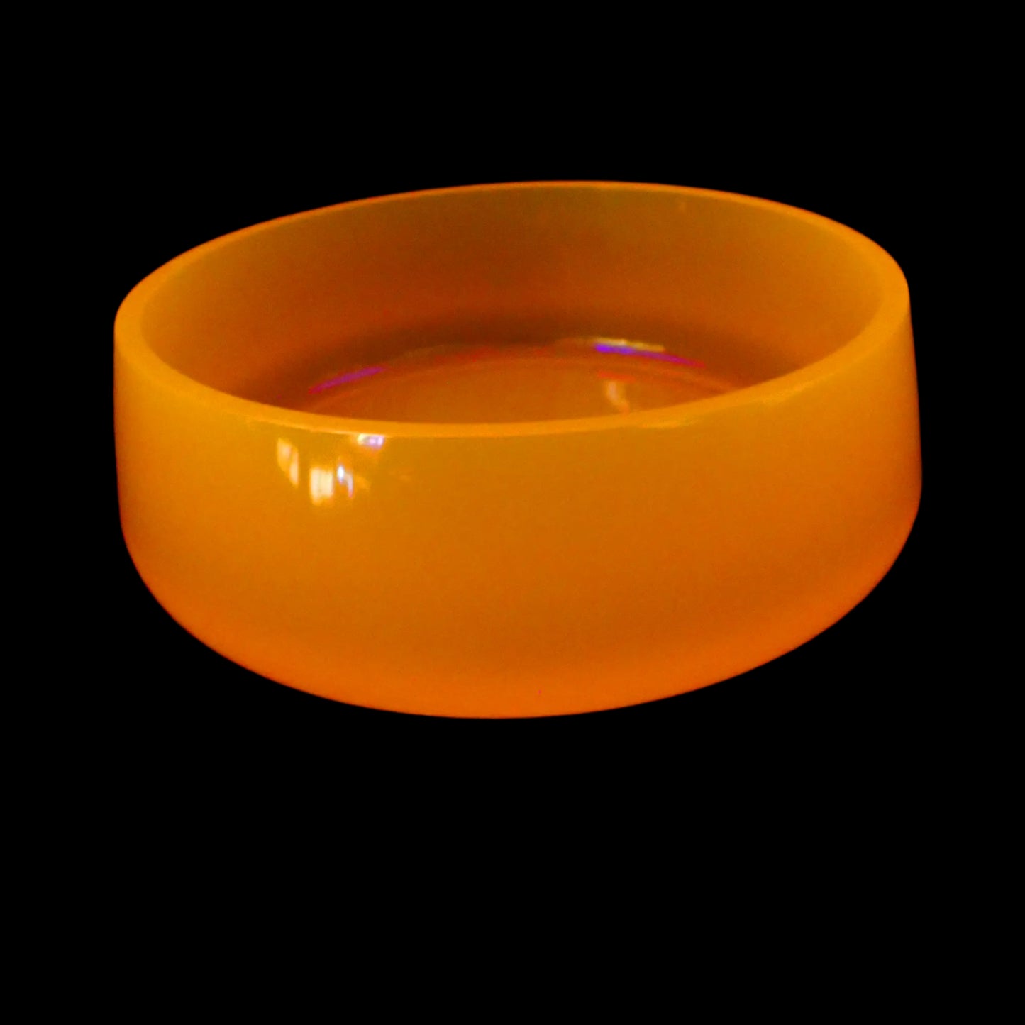 Image of the handmade neon orange resin decorative bowl showing how it is fluorescent under a UV light and glows a bright orange color.