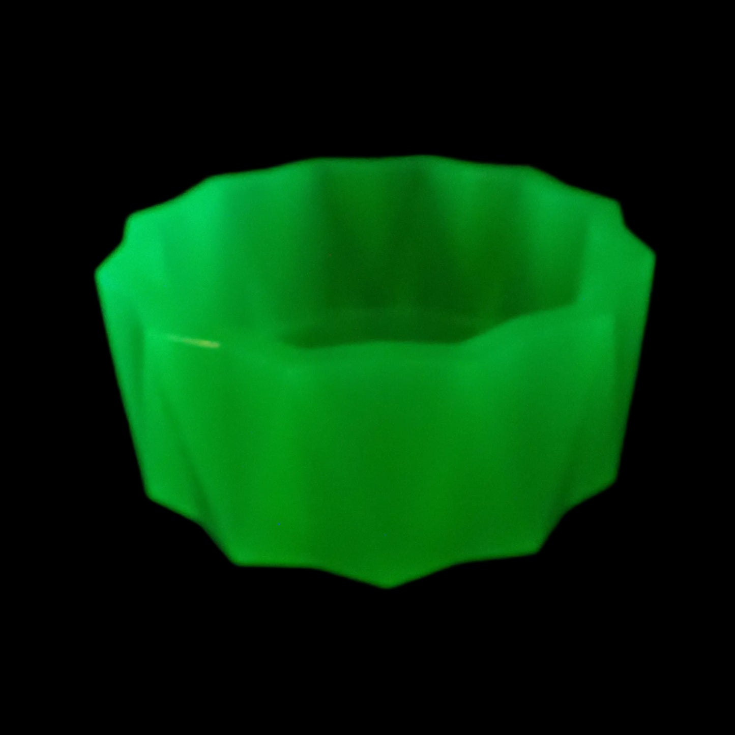 Image of the handmade neon green resin faceted large decorative bowl under a UV light to show that it is fluorescent in a bright green color.