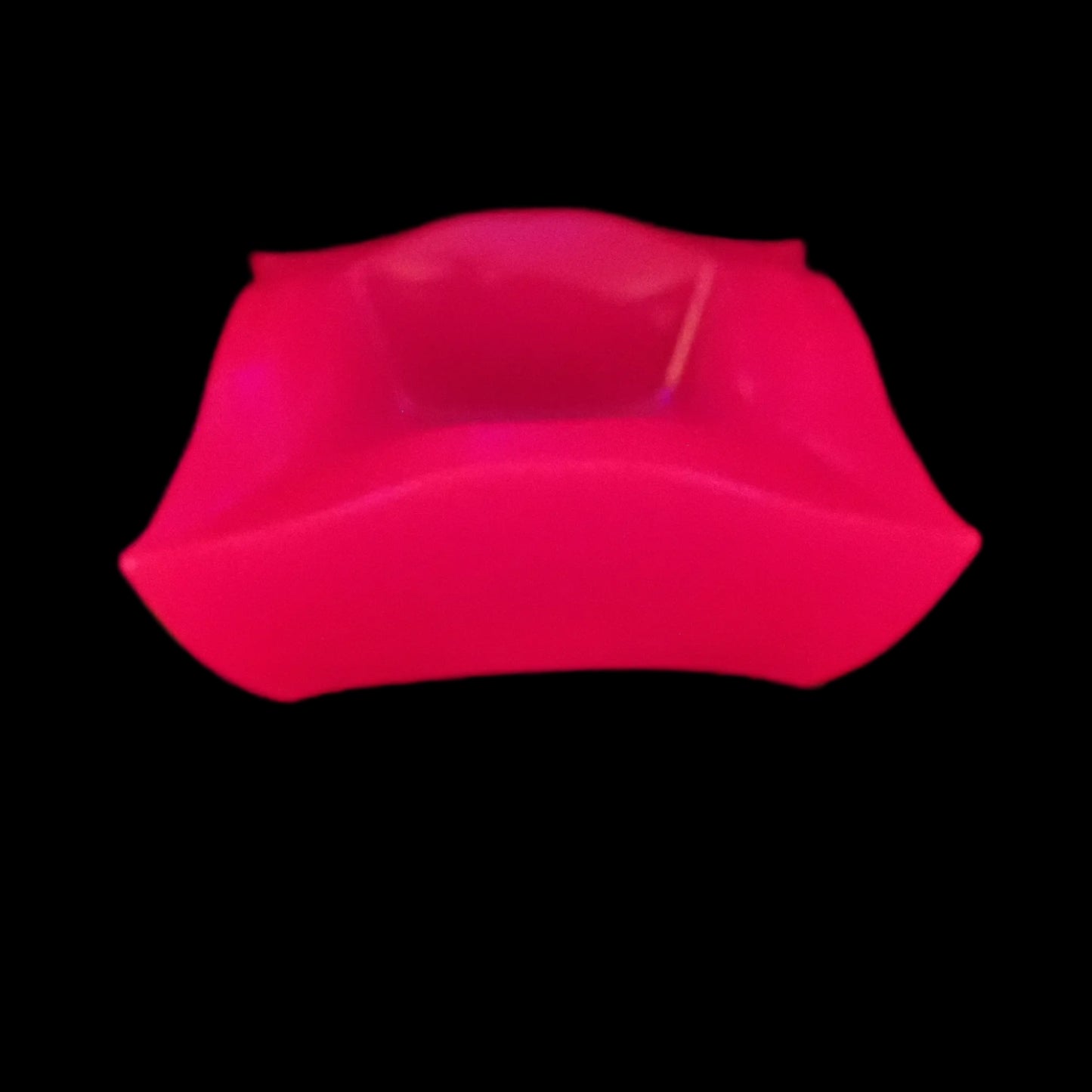 Image of the large handmade neon pink resin retro atomic style decorative bowl under a UV light showing that it is fluorescent and glowing a bright pink in color.
