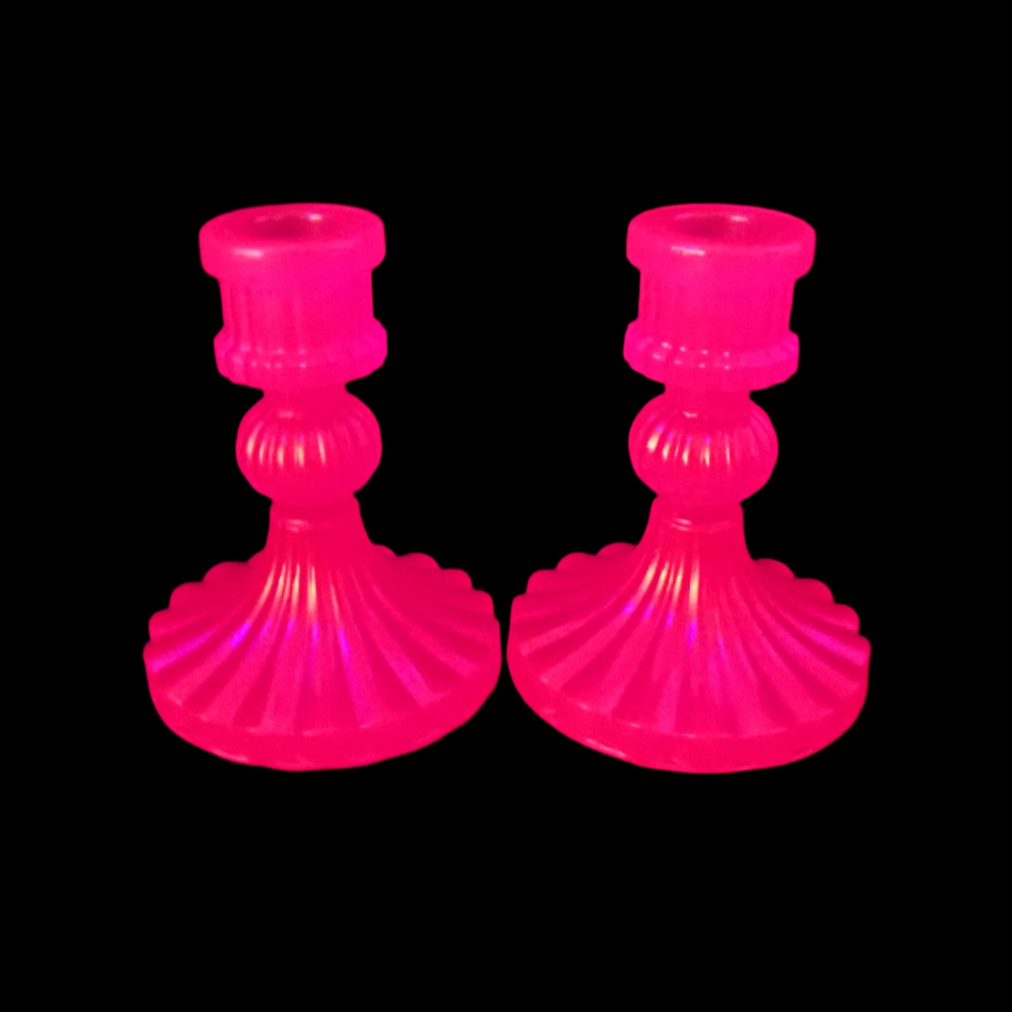 Image of the handmade neon pink resin candlestick holders under a UV light showing that the candle holders are glowing a bright pink in color.