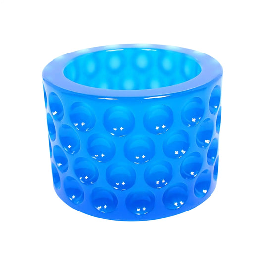 Side view of the decorative handmade resin trinket dish. It has a round cylindrical shape with an indented dot pattern all the way around it. The resin is a semi translucent neon blue color.