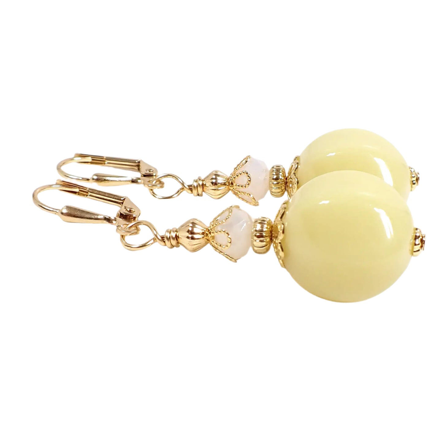 Angled view of the handmade beaded earrings. The metal is gold tone in color. There is a white faceted glass bead at the top. The bottom bead has a nugget like shape and is a light pastel lemon cream yellow color. The acrylic beads are opaque.