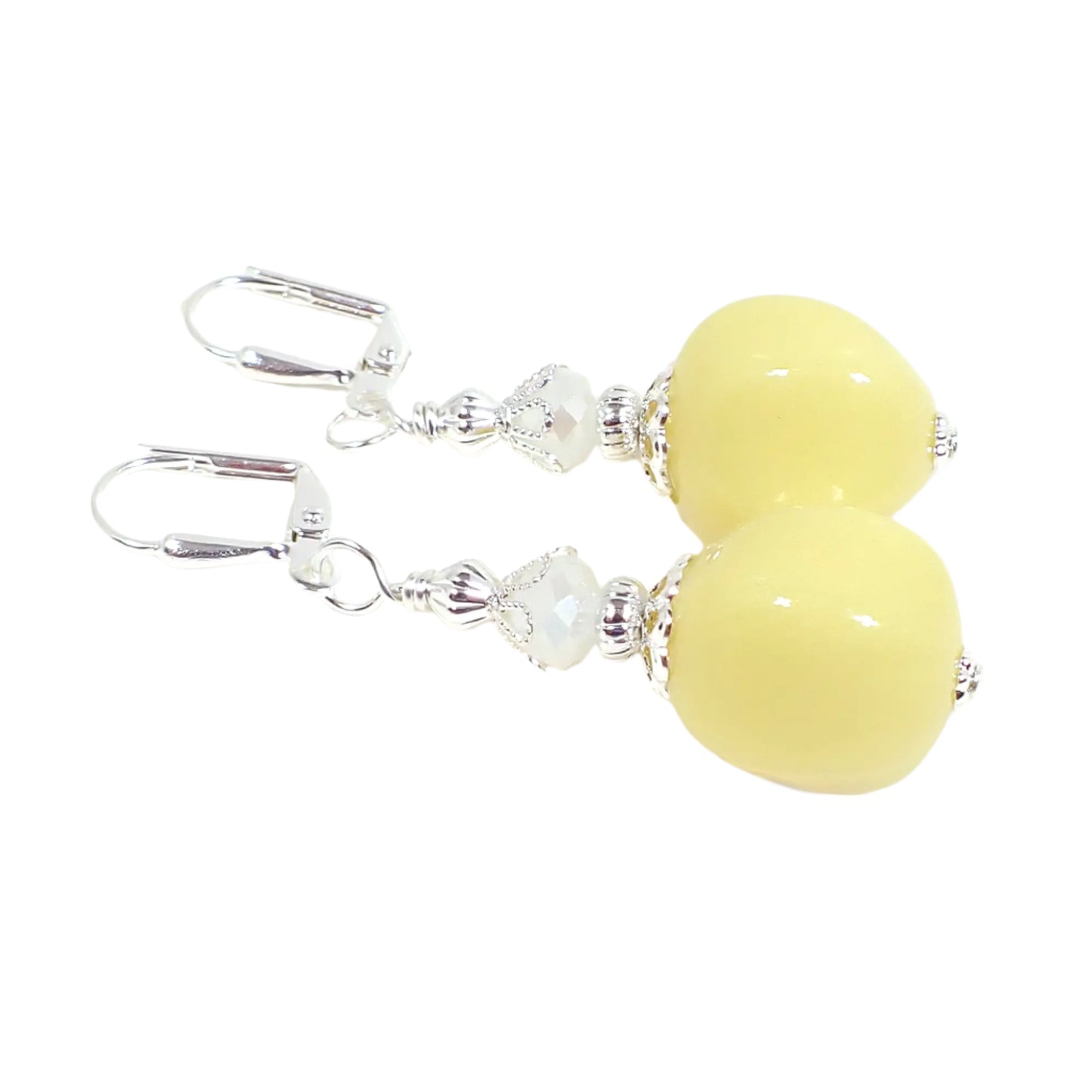 Angled view of the handmade beaded earrings. The metal is silver tone in color. There is a white faceted glass bead at the top. The bottom bead has a nugget like shape and is a light pastel lemon cream yellow color. The acrylic beads are opaque.