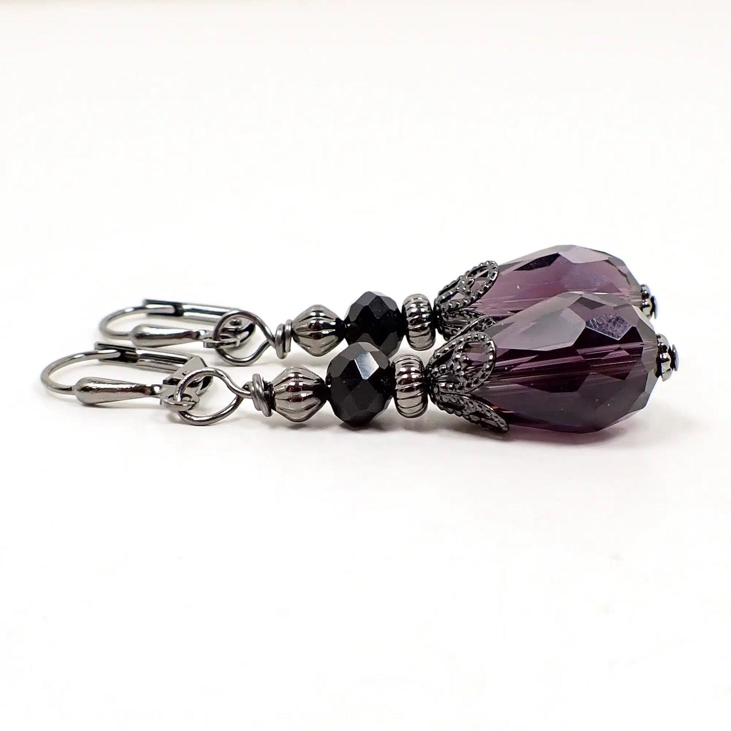 Side view of the handmade purple and black teardrop earrings. There are spacer beads and a filigree bead cap for a vintage style appearance and Goth look to the earrings.