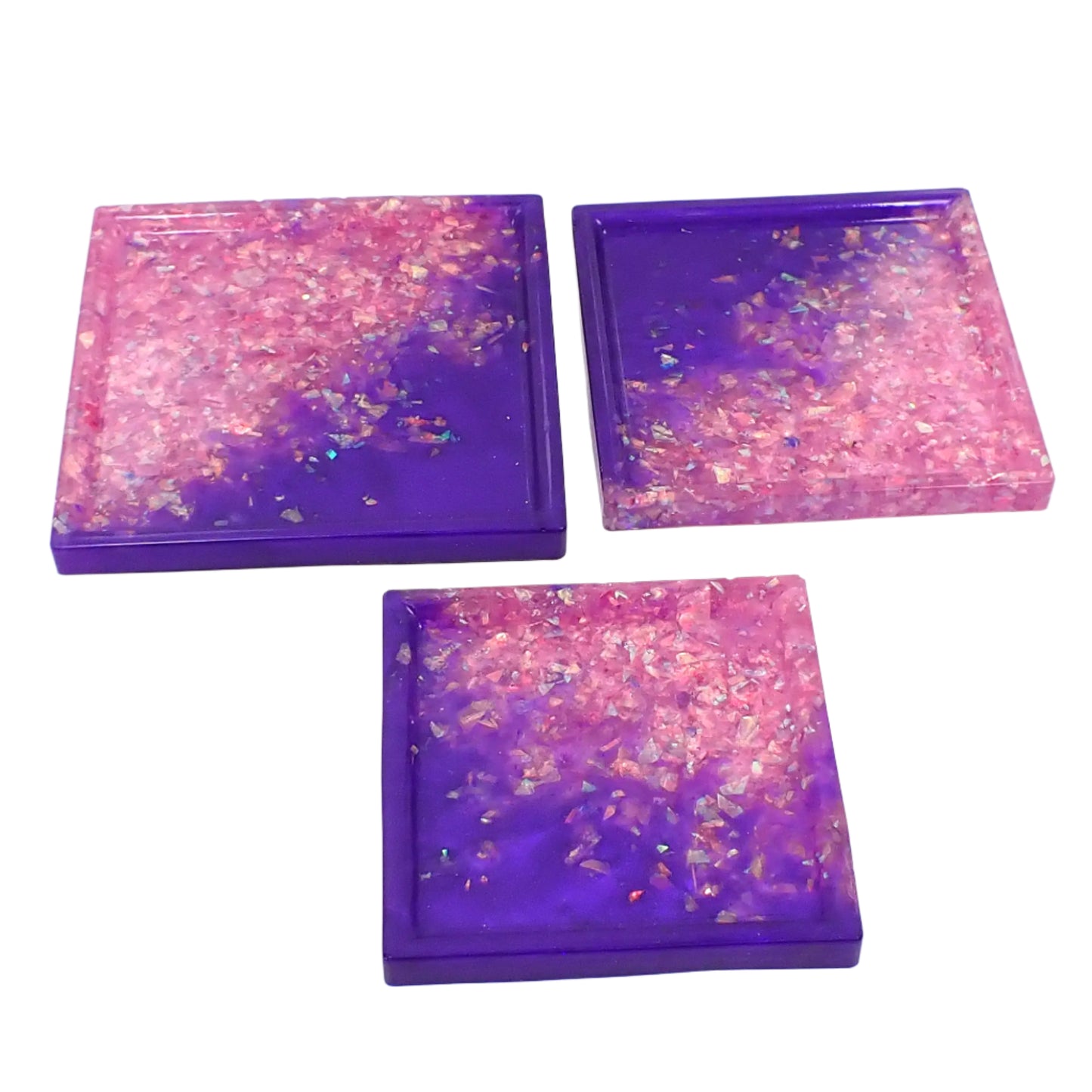 Photo showing the set of three small handmade resin trays. They are square with bright pearly purple resin and iridescent pink and purple glitter flakes. The design is mostly the pearly on one side at an angle and the flakes on the other.