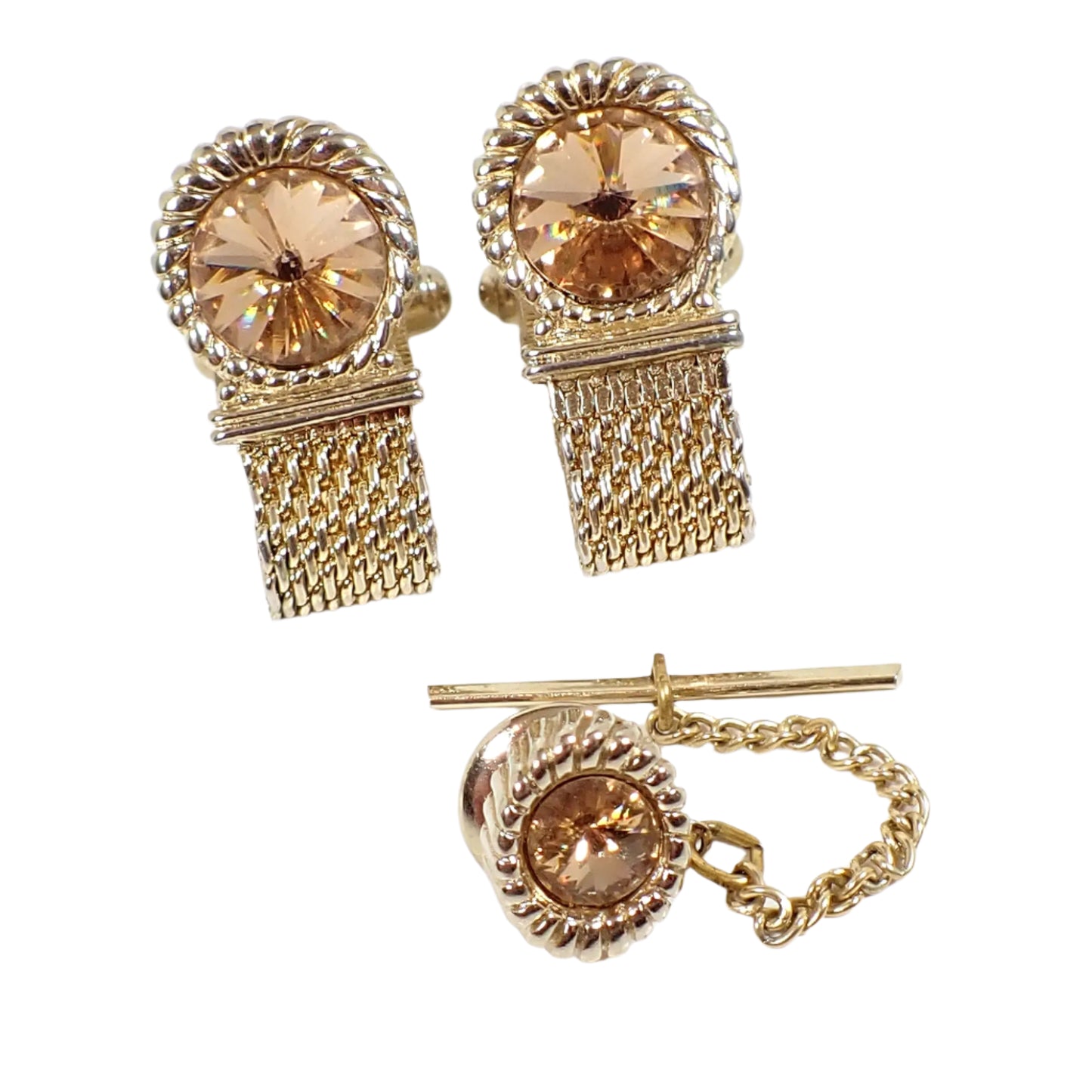 Front view of the Swank Mid Century vintagemens jewelry set. There is a pair of cufflinks at the top of the image and a tie tack at the bottom. The metal is gold tone in color. The cufflinks are round with mesh wrap around straps. The tie tack is oval. Each piece has a rivoli rhinestone in a champagne color.