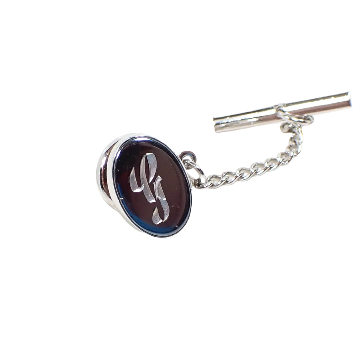Another full view image of the Mid Century vintage initial tie tack. Here the clutch chain with bar on the end is shown. The front of the tie tack is shiny and has reflections of something blue in the room showing on the side.
