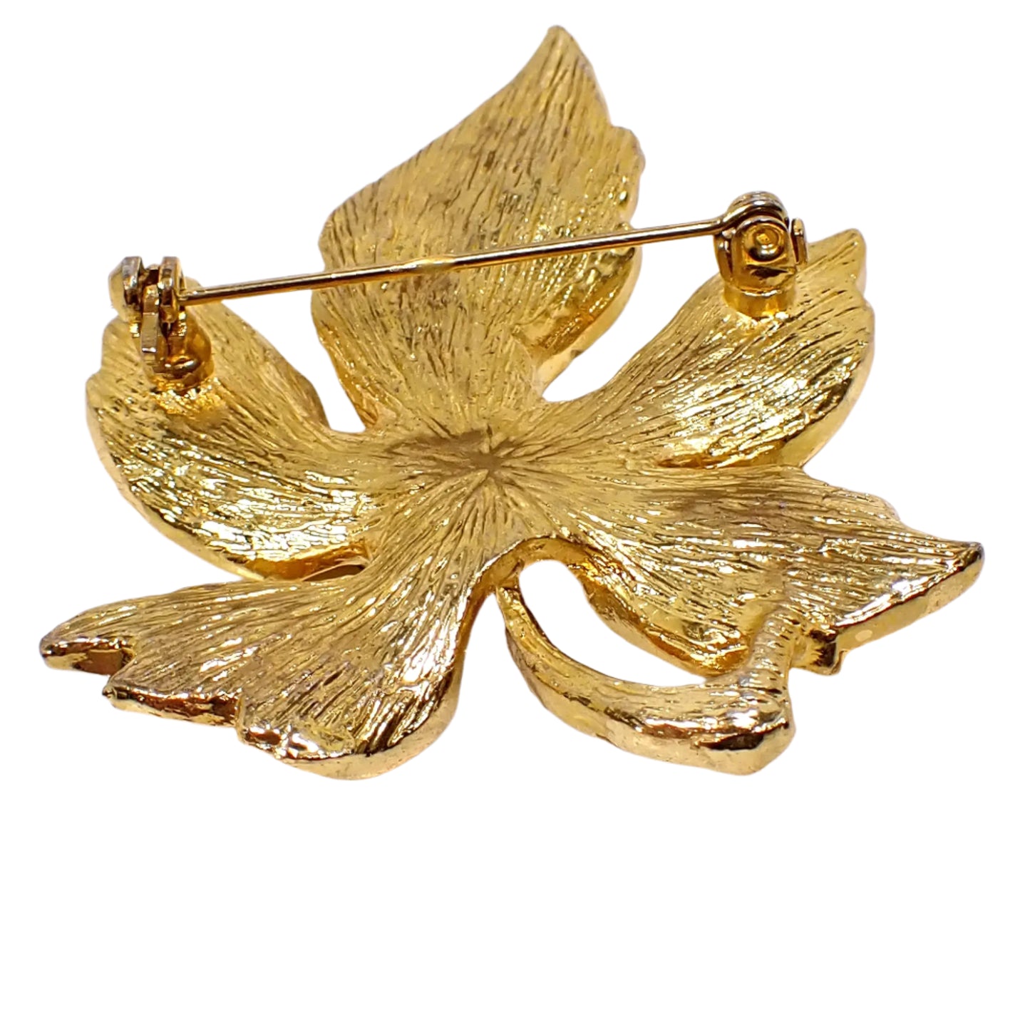 Photo of the backside of the brooch. Here the pin and clasp can be seen as well as the textured gold tone color metal on the back.