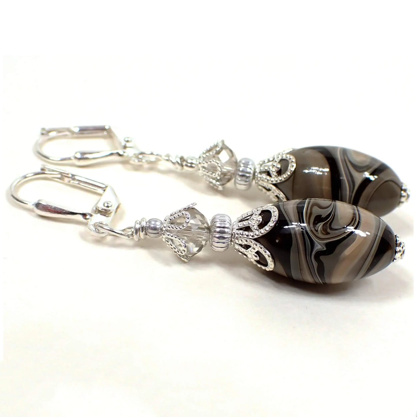 Side view of the handmade drop earrings with vintage lucite beads. The metal is silver plated in color. There are faceted glass crystal beads at the top in a very light gray color. The bottom oval beads are lucite and have a swirled marbled pattern with shades of gray, brown, black, and white. Each bottom bead is different in pattern from the other for a unique look.