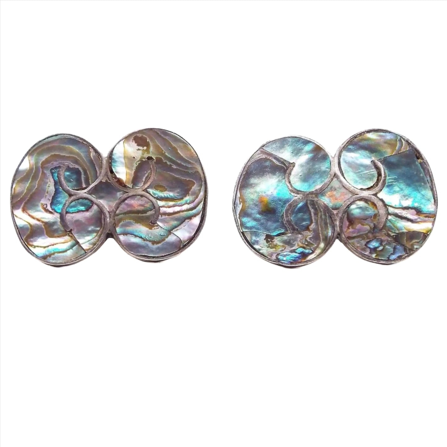 Front view of the Taxco 940 retro vintage screw back earrings. The metal is dark silver in color. Each earring has a shape that looks like two kidney beans facing each other. The inside area has inlaid abalone shell with multi color flashes of color.
