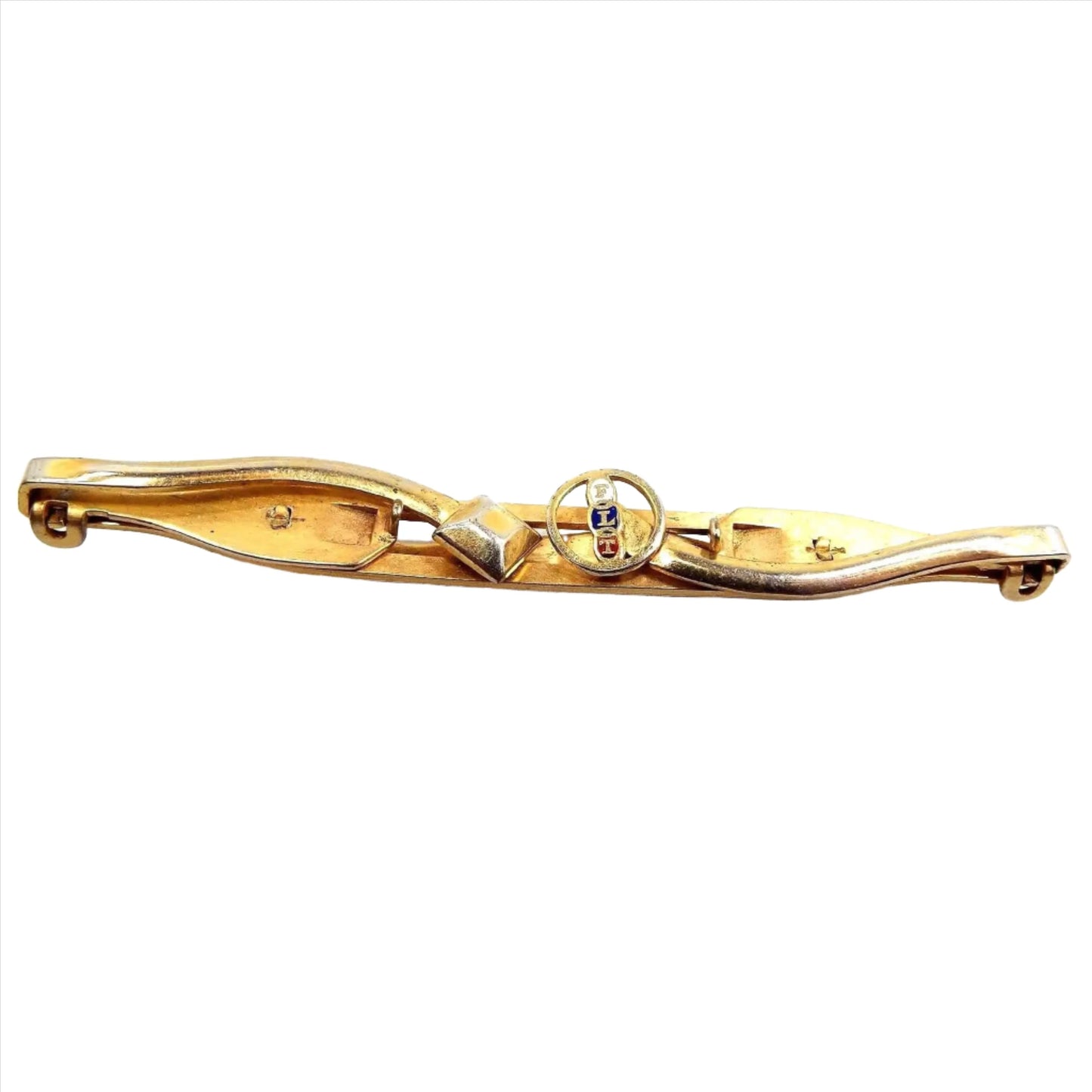 Top view of the Mid Century vintage Anson FLT Odd Fellows tie bar. It's long gold tone in color with each side that opens out as a clip. The left side has a diamond shape at the end and the right side has an open circle with FLT going down the middle of it. The letters are enameled with white, dark blue, and red.