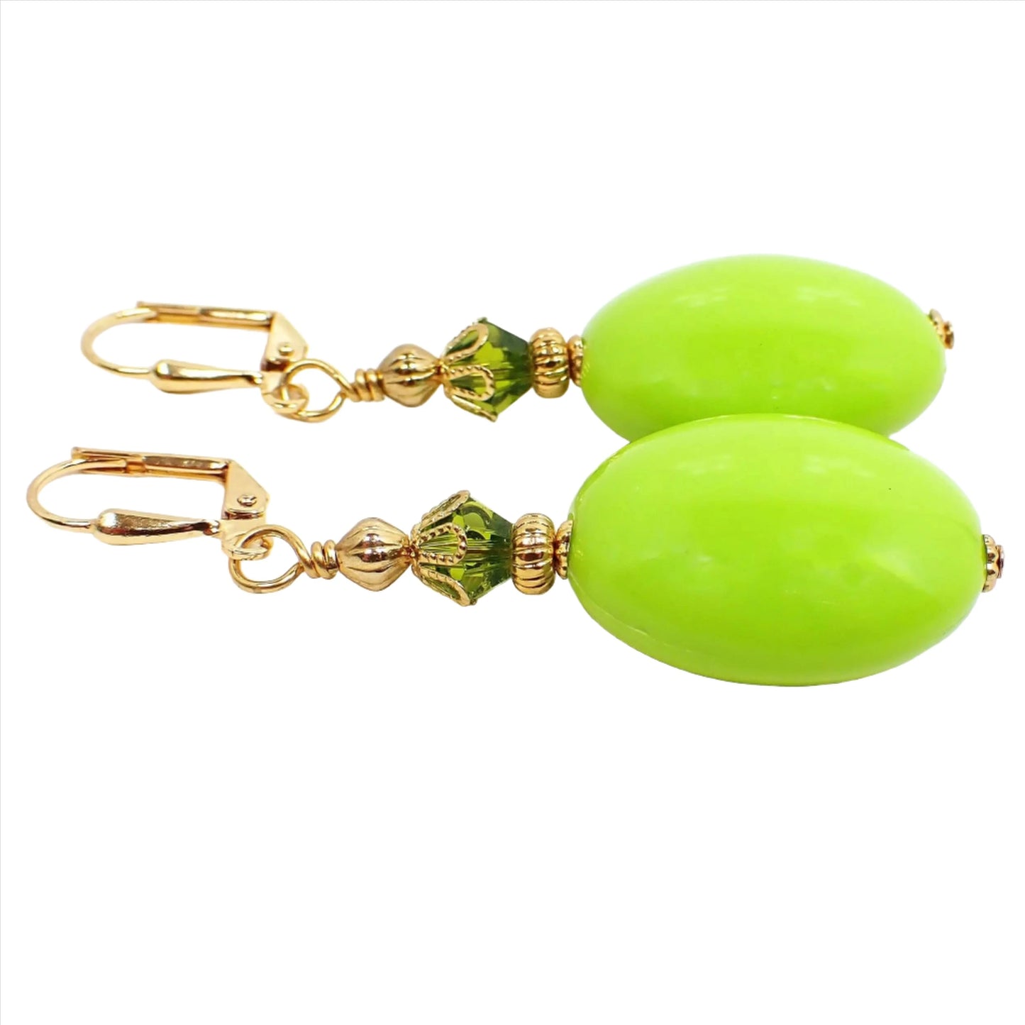 Angled view of the large handmade acrylic drop earrings. The metal is gold plated in color. There is a faceted green glass crystal bead at the top and a large oval vintage acrylic bead in lime green on the bottom.