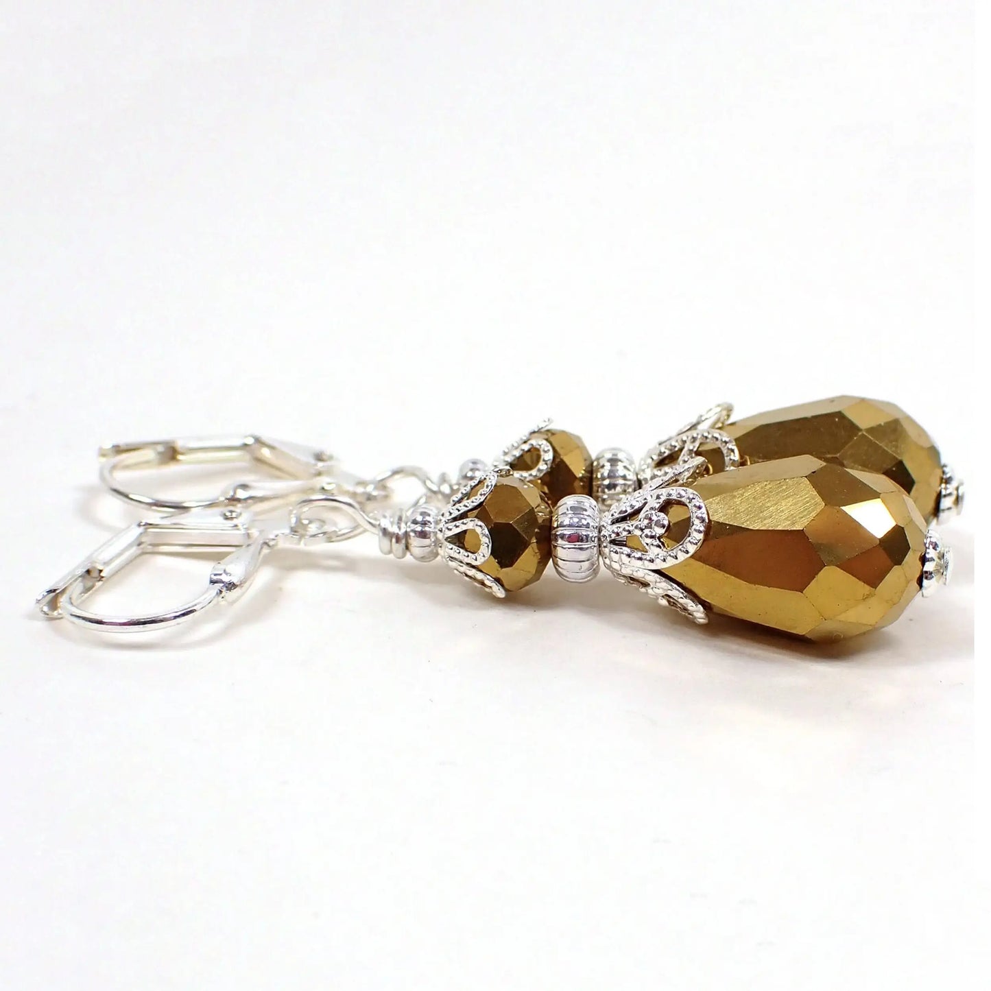 Side view of the handmade teardrop earrings. The metal is silver plated in color. There are faceted glass rondelle beads at the top and teardrop shaped beads at the bottom. The beads are a dark metallic antiqued gold in color.