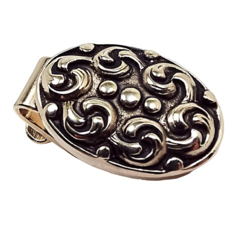 Front view of the small Mid Century vintage tie clip. It is a small oval shape and has antiqued gold tone color on the front. There is a raised feather and dot like design.