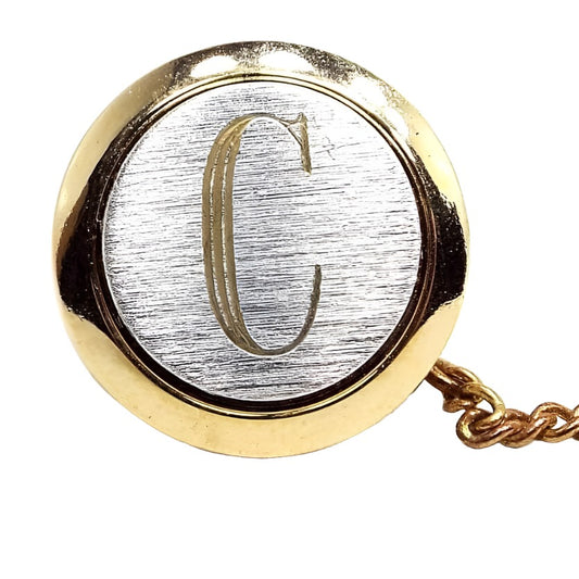 Enlarged front view of the retro vintage initial tie tack. It is round and has a brushed matte silver tone front with a gold tone edge. There is a gold tone letter C engraved on the front in fancy block style letter.