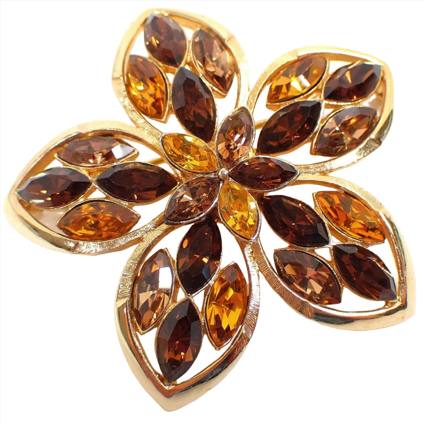 Angled front view of the Mid Century vintage rhinestone floral brooch pin. The metal is gold tone plated in color. There are five rounded petals with pointed ends. Each petal and the middle of the flower has marquis shaped rhinestones in brown, orange, and dark yellow color.