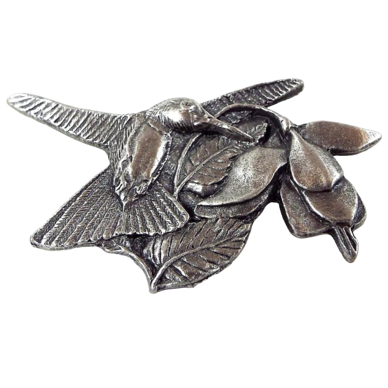 Front view of the retro vintage Birds and Blooms Premiere Edition brooch pin. It is made of pewter and gray in color. There is a flying hummingbird flying next to a Fuchsia bloom that hangs down on the right side of the brooch.