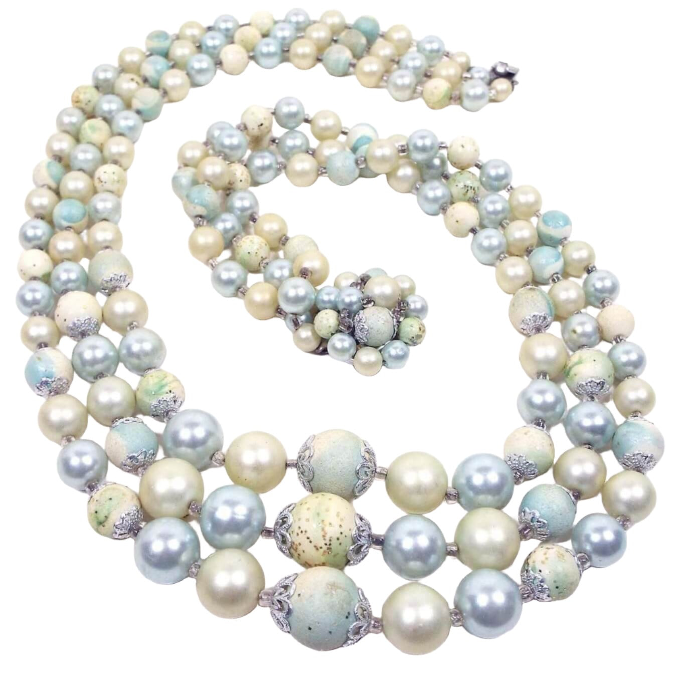 Top view of the Mid Century vintage Japan pastel beaded multi strand necklace. It has three rows of round plastic beads in light blue and yellow, along with some faux pearls in off white. There is a beaded box clasp at the end.