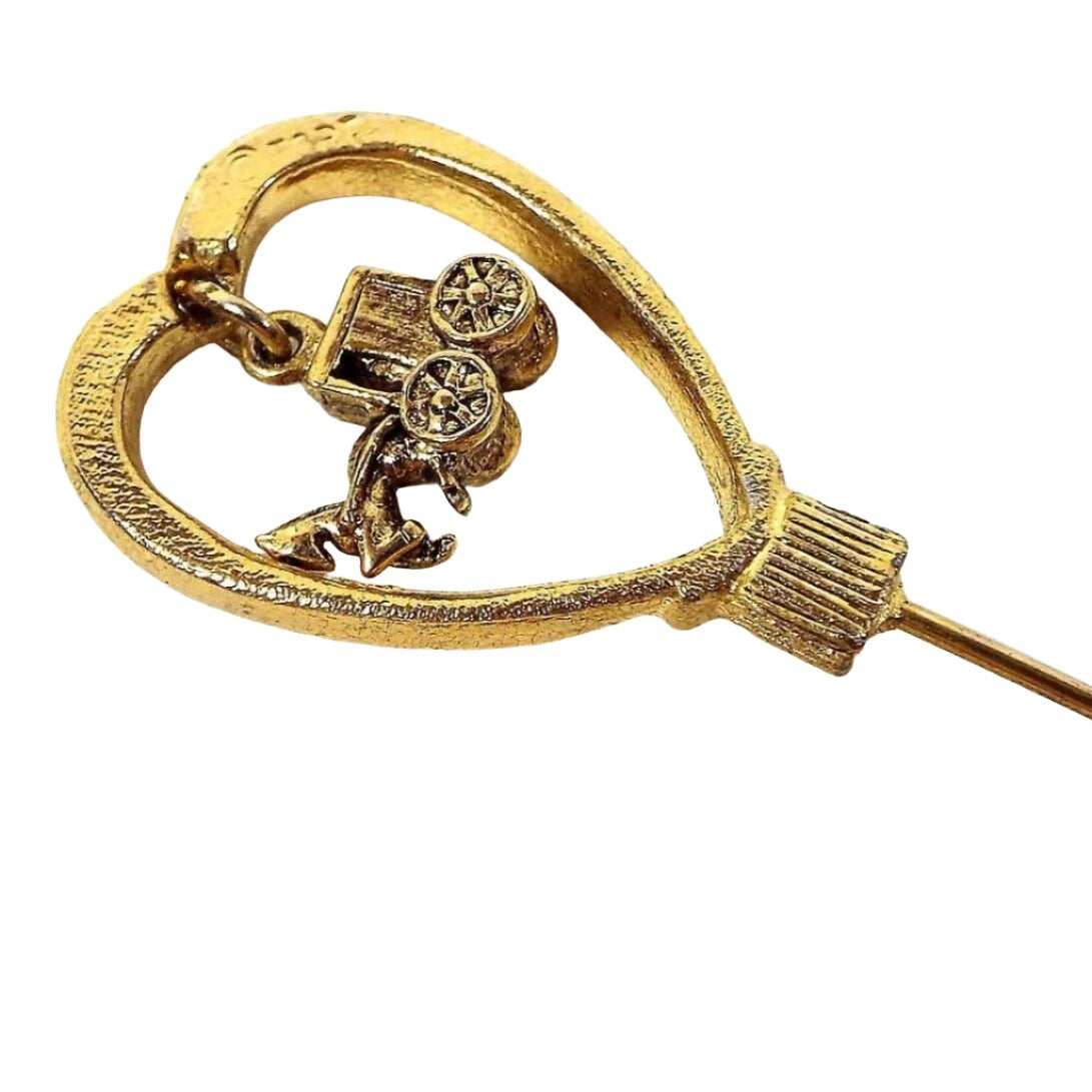 Enlarged top view of the retro vintage horse and carriage stick pin. The metal is gold tone in color. There is a large open heart at the top with a small dangling charm of a horse and buggy on the inside.