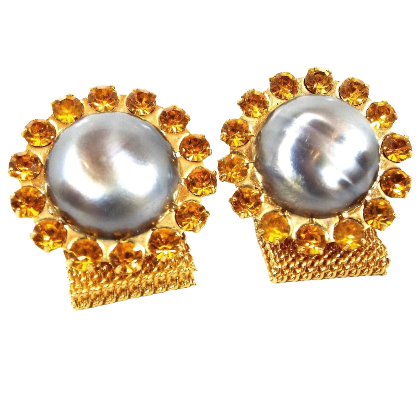 Front view of the Mid Century vintage rhinestone and faux pearl wrap around cufflinks. The metal is gold tone in color. There is a large round gray blue faux pearl cab in the middle surrounded by small orange rhinestones. There is a wide mesh chain coming from the bottom that goes around to the back.