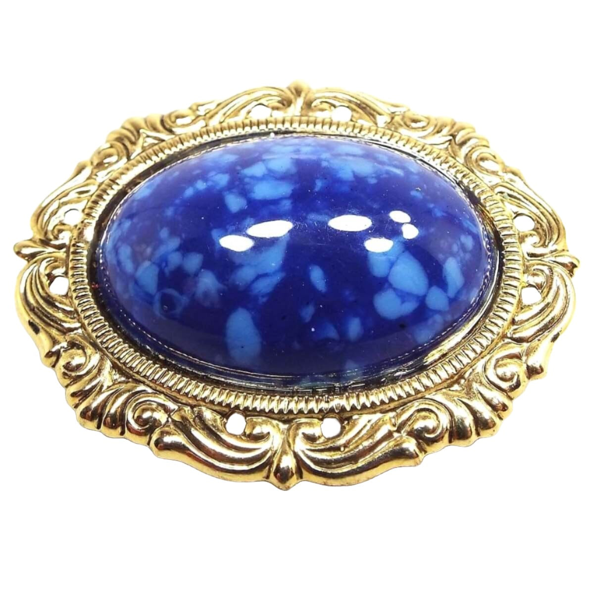 Front view of the retro vintage brooch pin. The metal is gold tone in color. It has an oval design with fancy style edge. The middle cab is a domed oval cab made of plastic that is dark blue with lighter blue speckles.