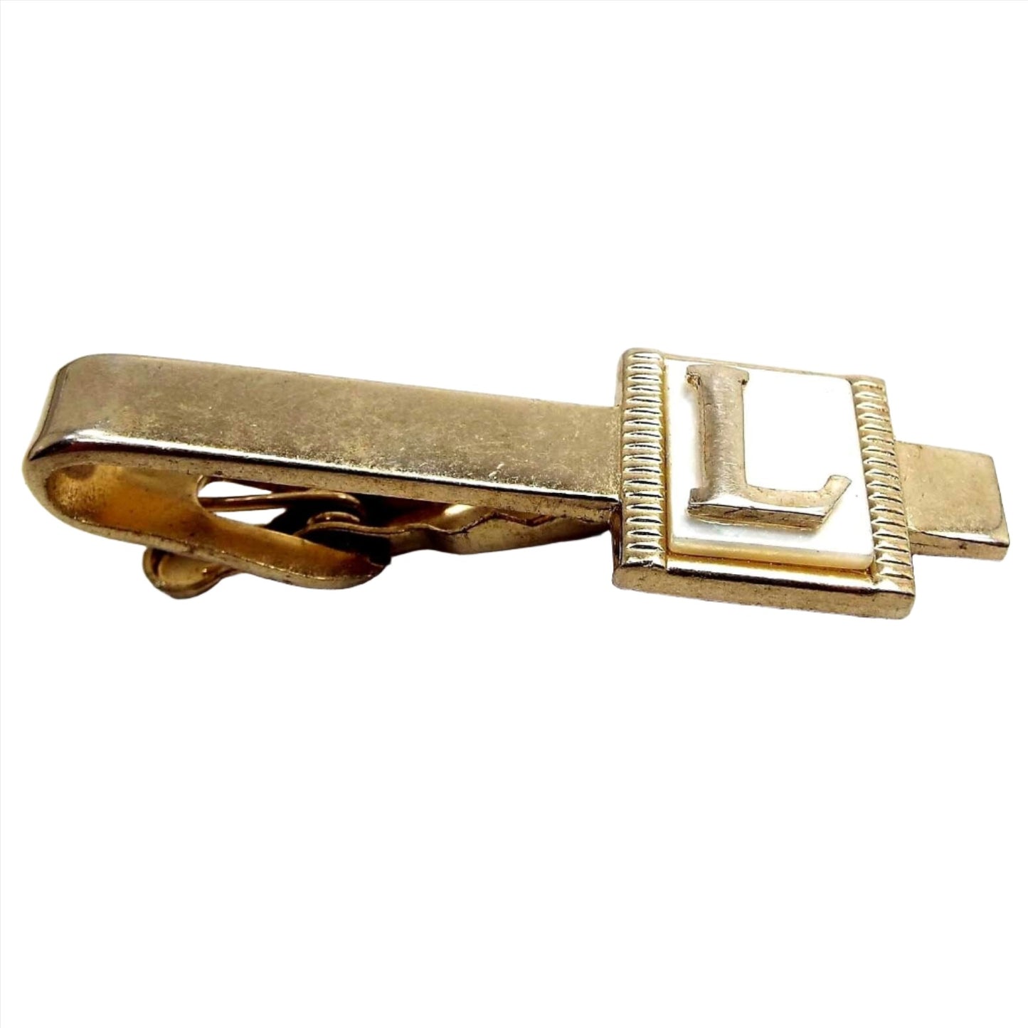 Angled top view of the Mid Century vintage initial tie clip. It is gold tone in color. There is a pearly white mother of pearl cab at the end with the letter L on it.