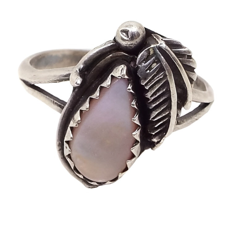 Front view of the retro vintage Southwestern style mother of pearl ring. The setting and band are a darkened silver tone in color. There is a bezel set teardrop mother of pearl shell cab that is a light pink in color. On the side of the bezel is a feather shaped piece of metal and a dot of metal at the top.