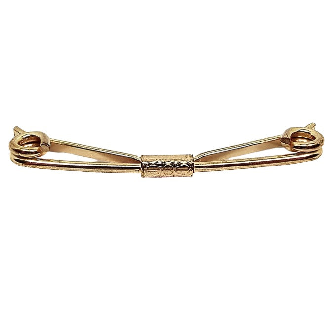 Angled front and side view of the 1940's Mid Century vintage collar clip. It is gold tone in color and has spiral ends and a bow tie stamped design in the middle.