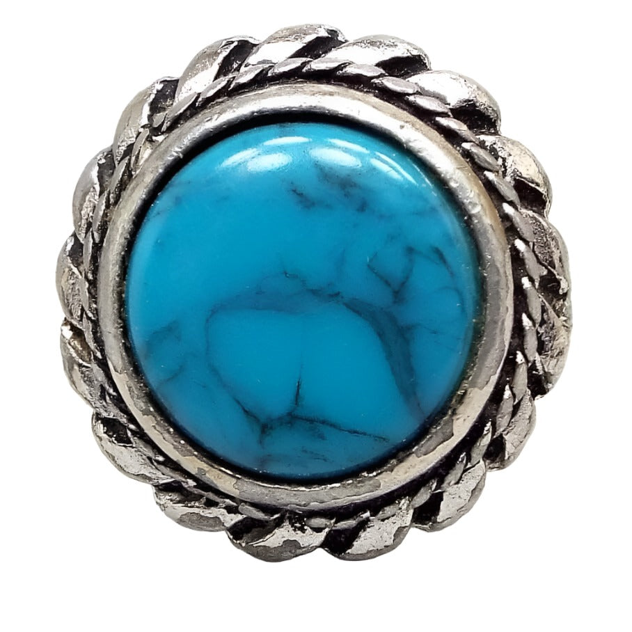 Front view of the retro vintage Southwestern style faux turquoise ring. The front setting is silver tone pewter and has a braided rope design on the outside edge of the bezel. The outer edge has a sort of short pinwheel style design. The middle cab is blue with gray and black lines marbled in. Chips from the silver plating can be seen on the setting and edges.