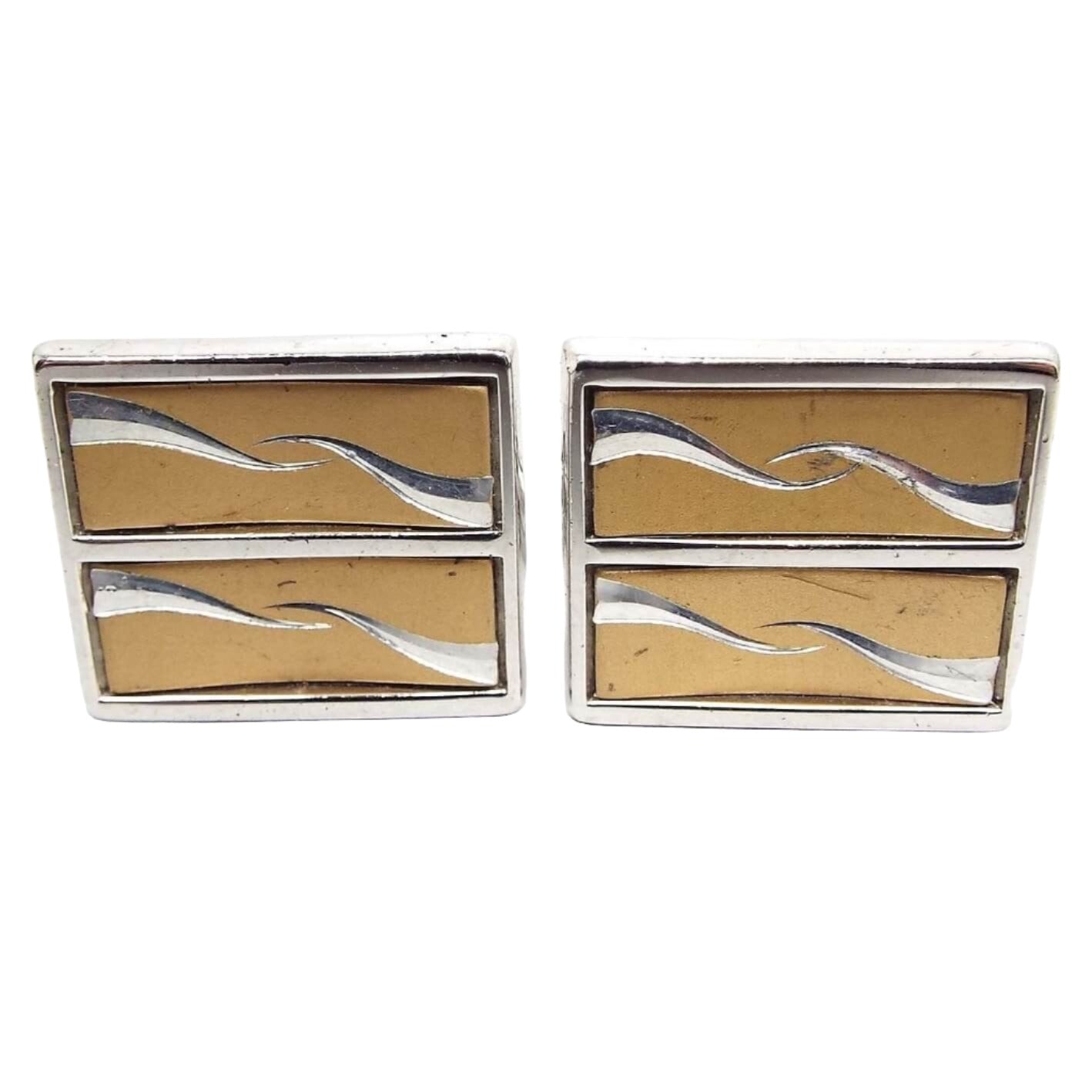 Front view of the retro vintage Anson two tone cufflinks. They are square in shape with the front being divided into two rectangle areas with wavy spikes pointing towards the middle. The metal is mostly silver tone in color with an antiqued gold tone color background.
